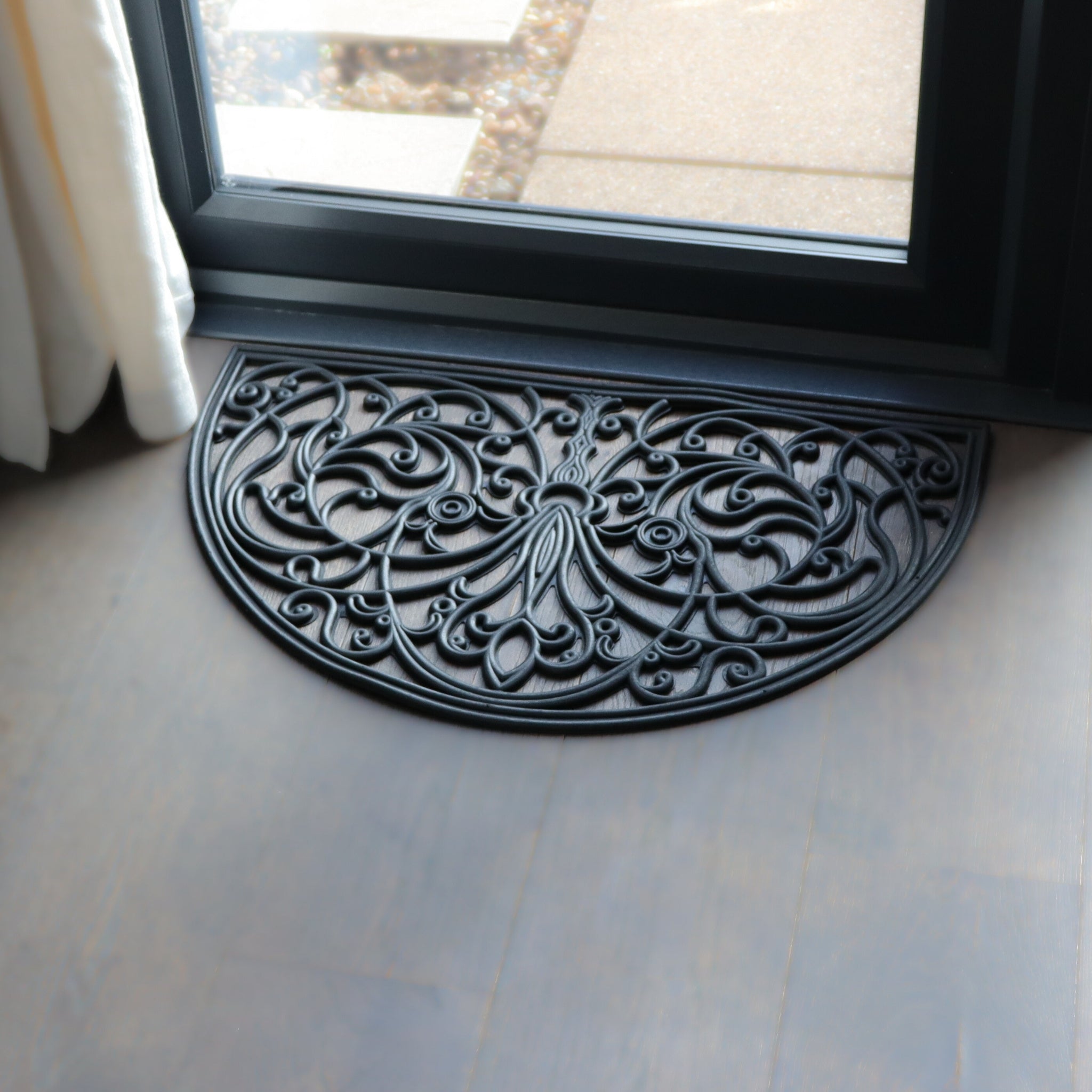 Decorative black doormat with intricate patterns on a light wooden floor.
