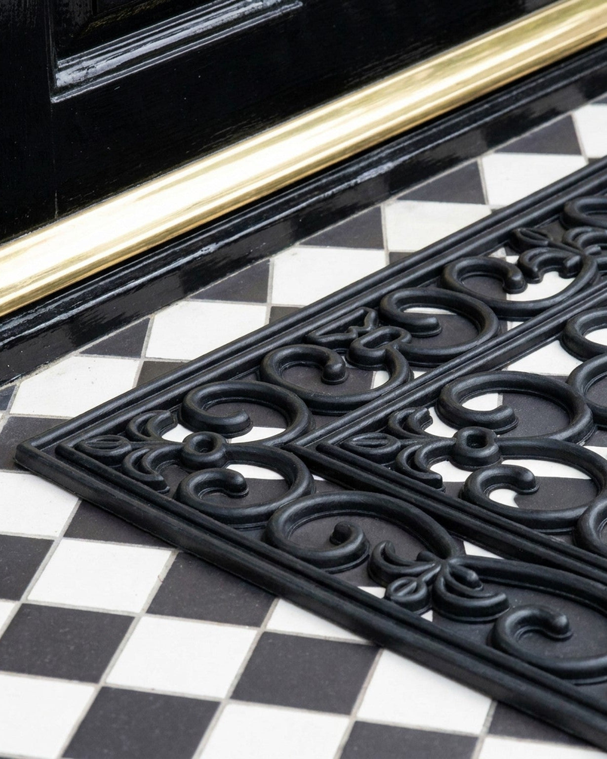 Decorative black doormat with intricate patterns on a checkered floor.