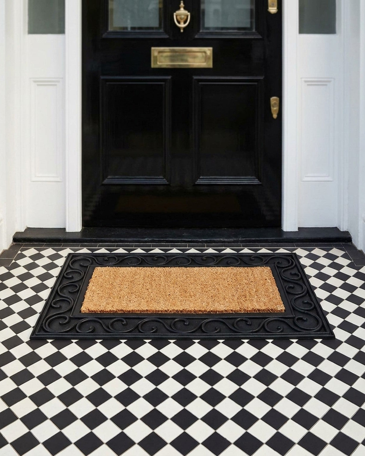 Black door with gold handle and mail slot, black and white checkered floor, and decorative doormat.