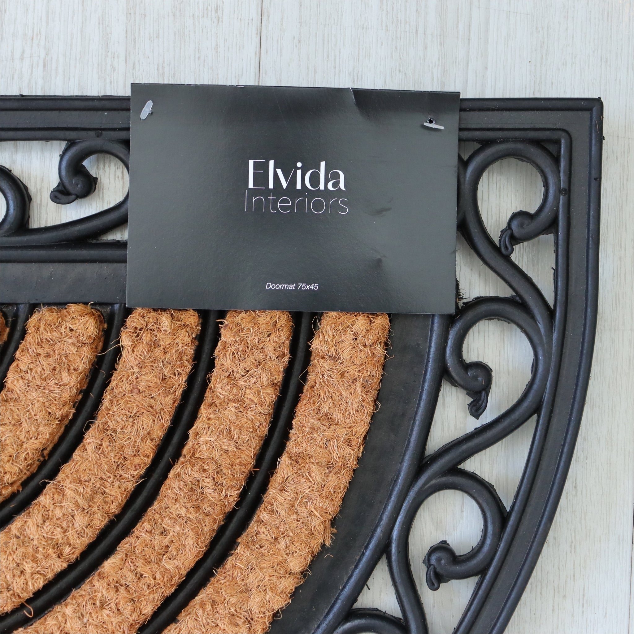 Decorative doormat with ornate black metal frame and 'Elvida Interiors' sign.