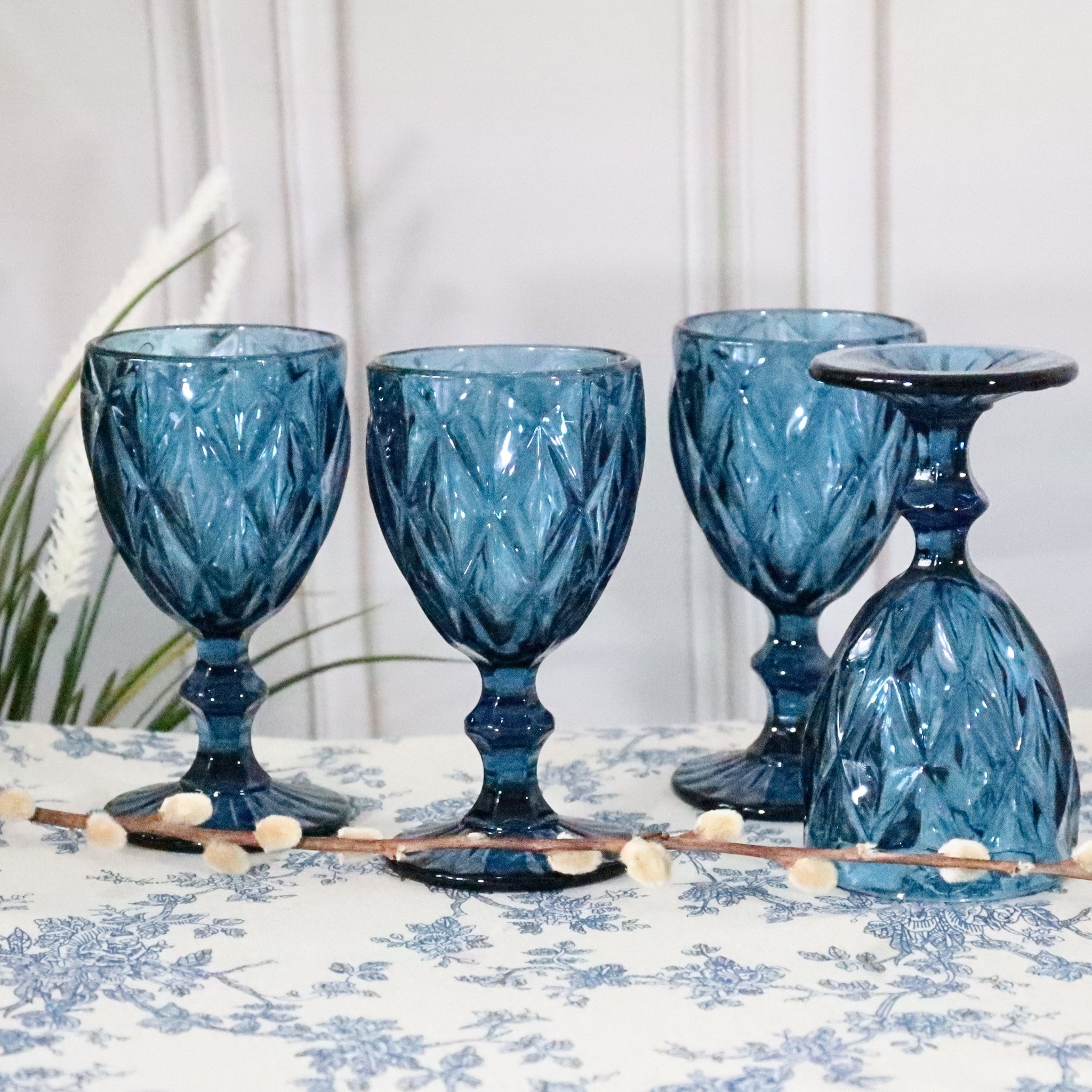 Set of four blue glass goblets on a decorative tablecloth with a white background