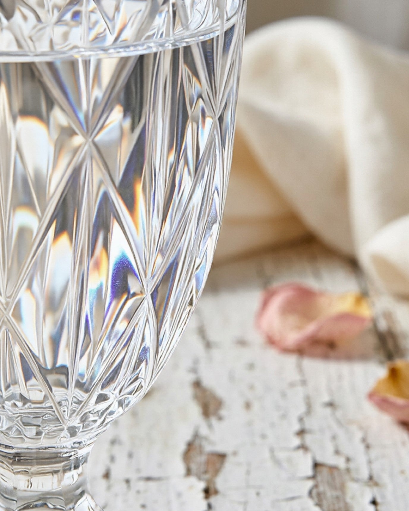 Close-up of a crystal glass with a blurred background featuring a white cloth and dried flowers.