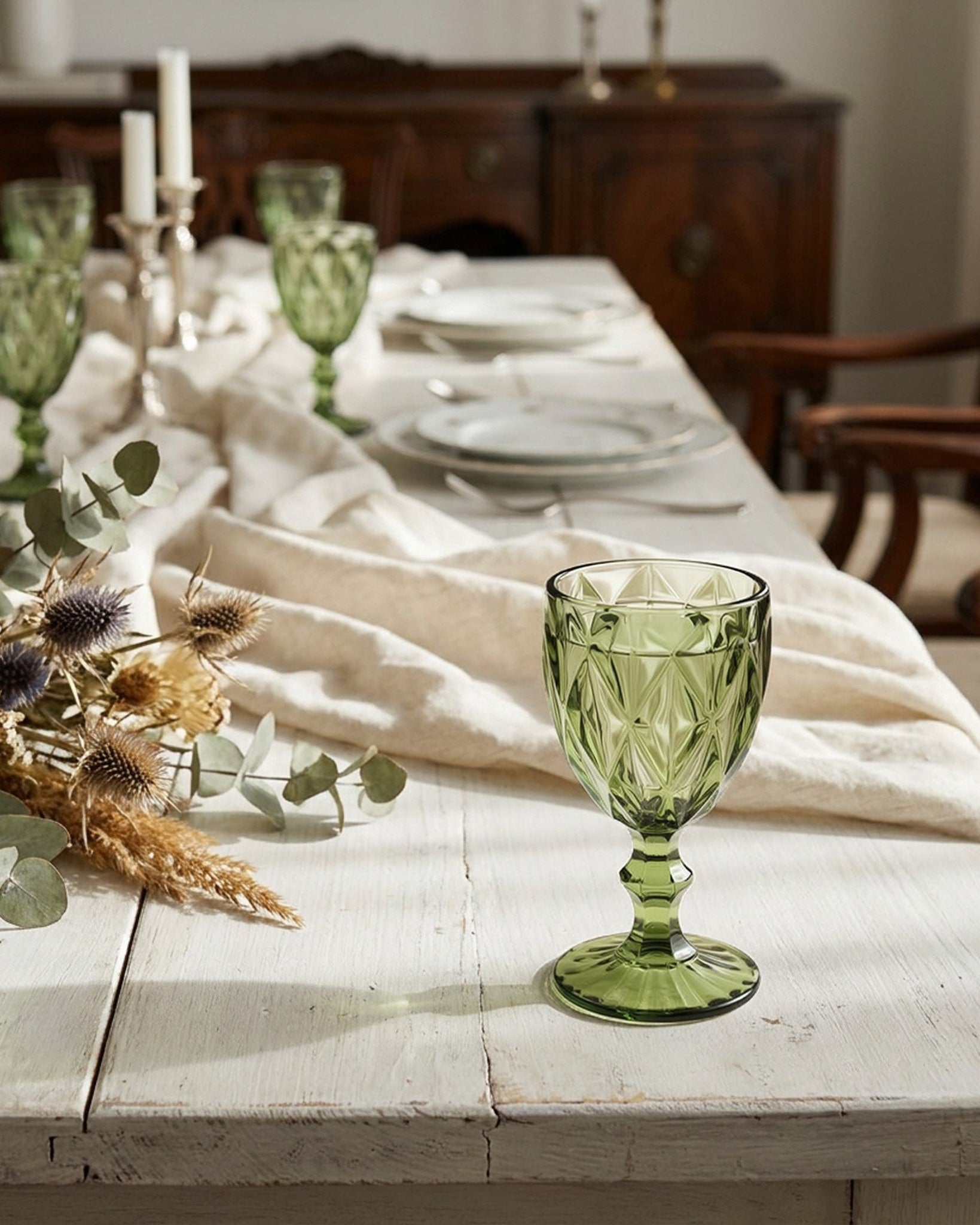 Green glass goblet on a rustic wooden table with a floral arrangement.