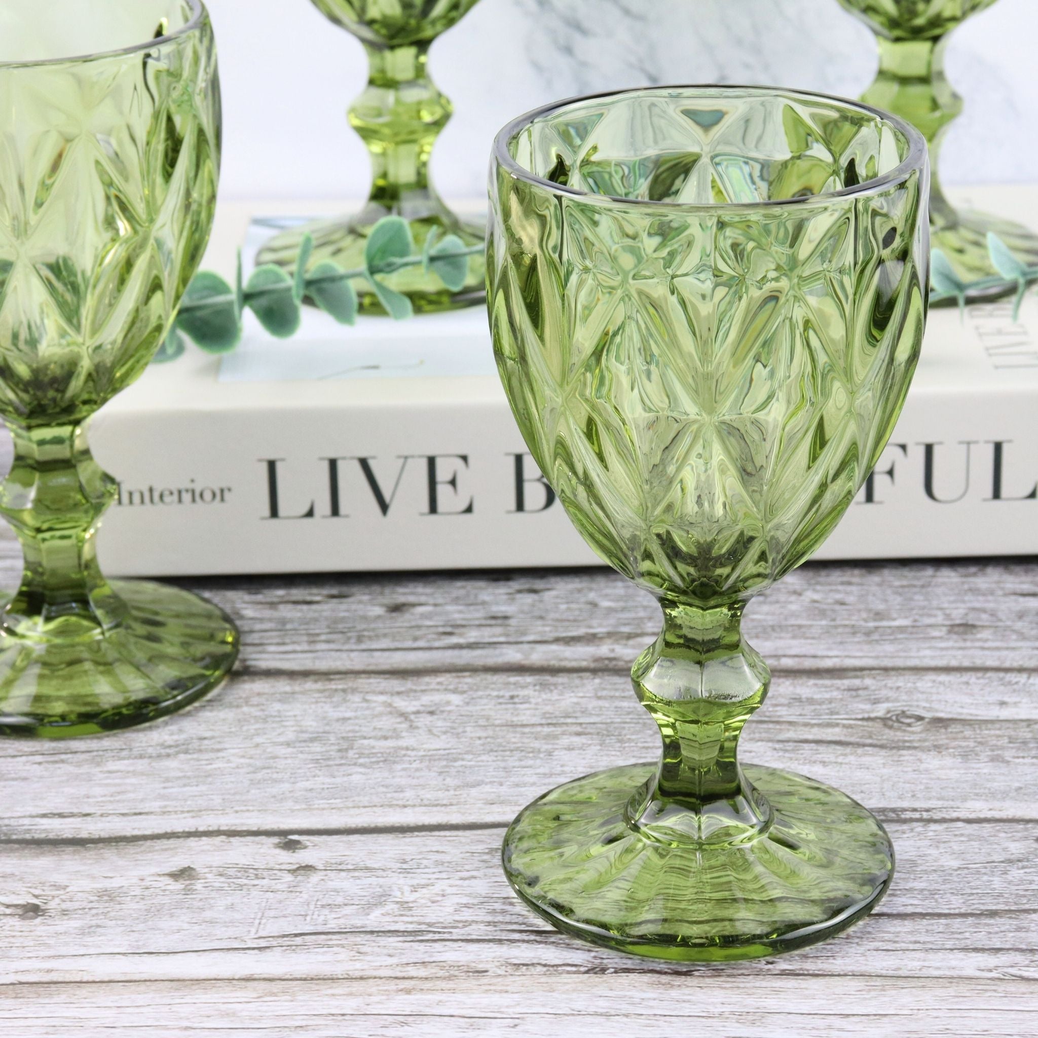 Set of green glass goblets on a decorative surface with a blurred background