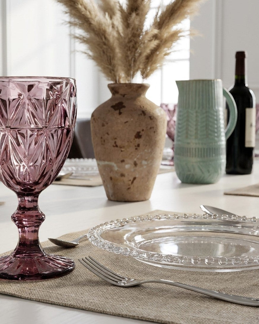 Dining table setting with a pink glass, silverware, and decorative items.