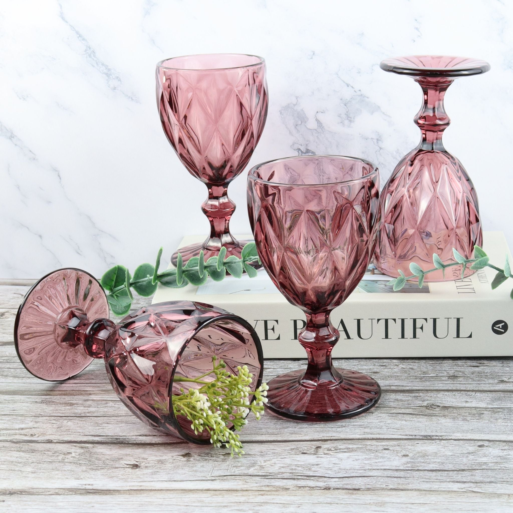 Set of purple glass goblets on a wooden surface with an orange flower.