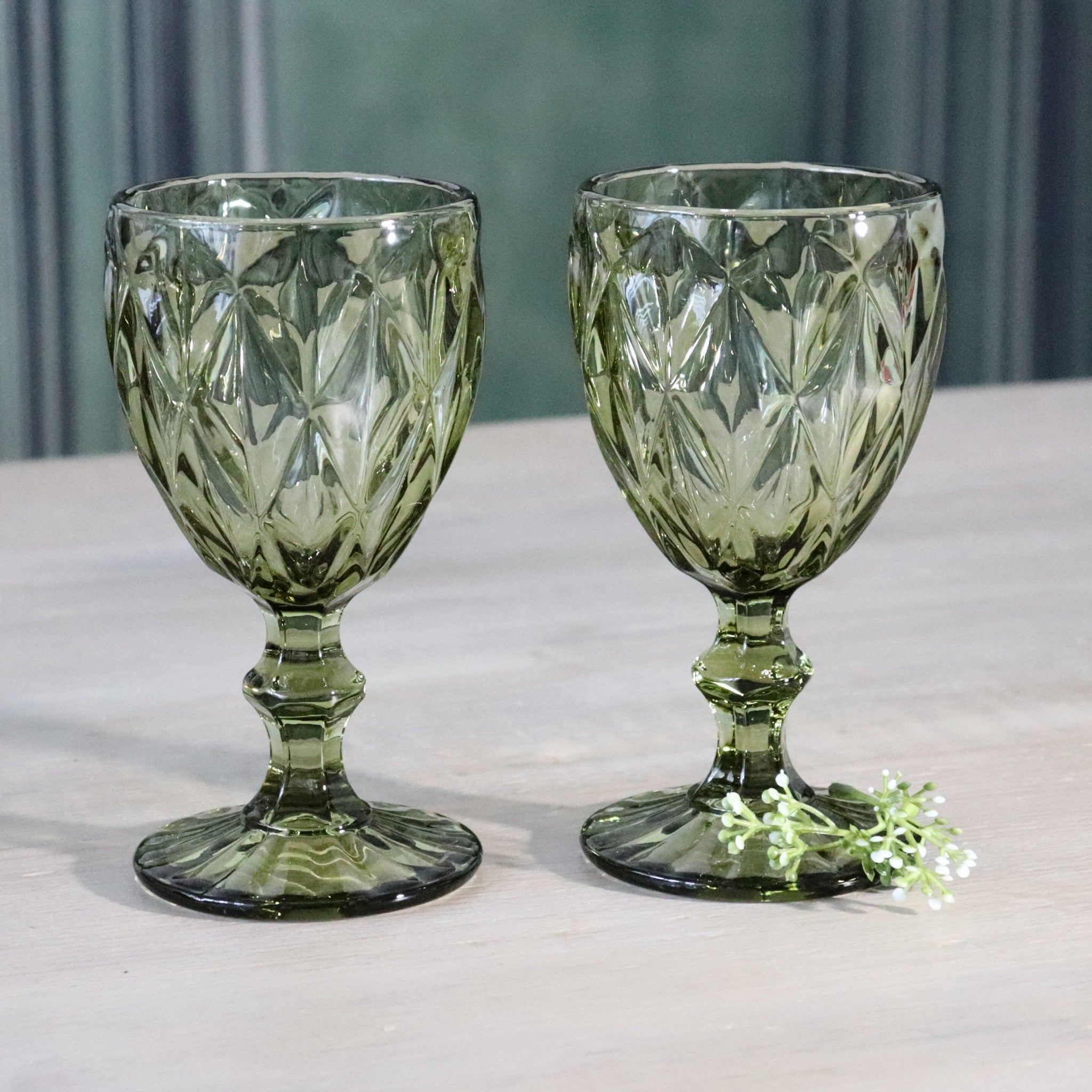 Luxury green glass wine goblet with intricate design on a reflective surface