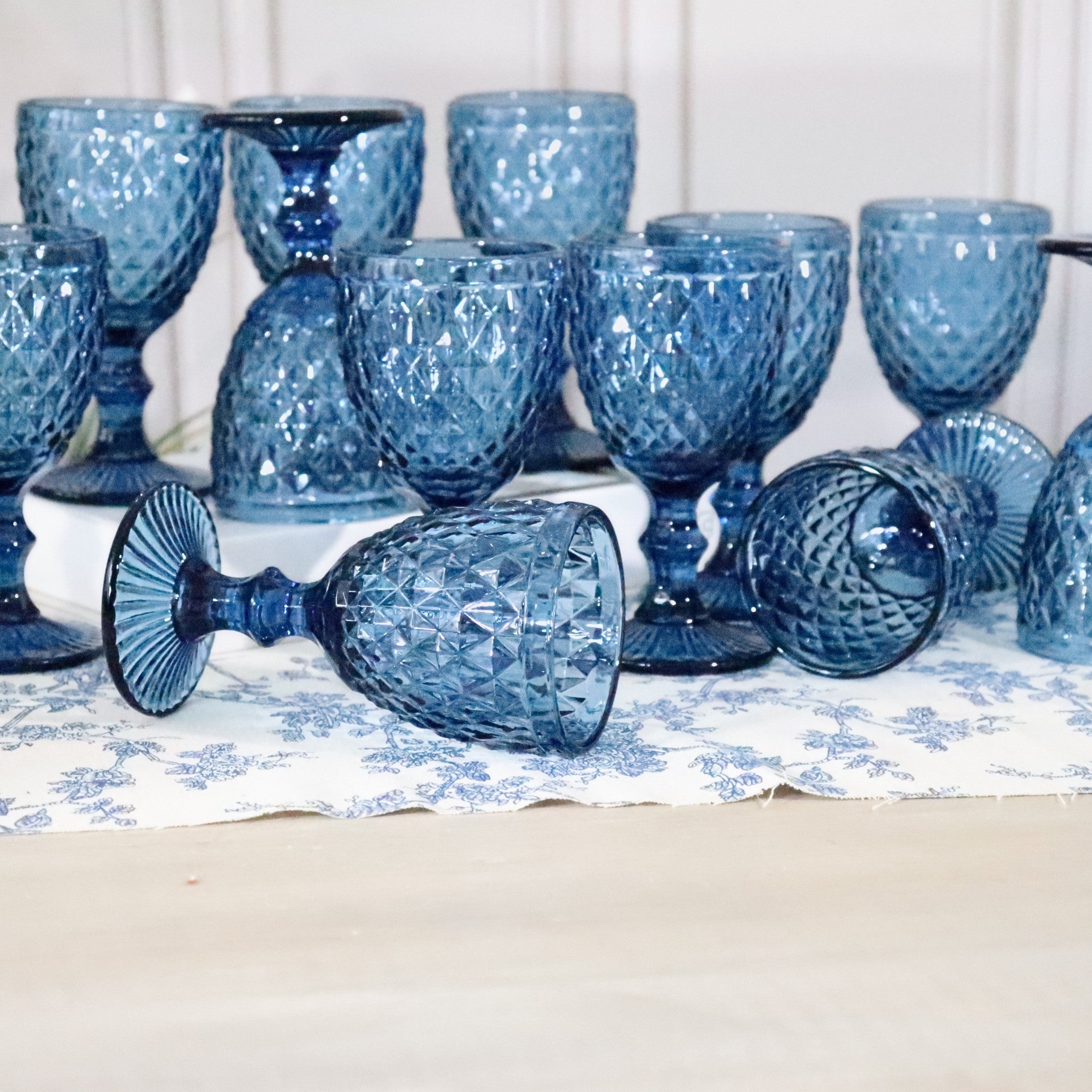 Set of blue glass goblets on a table with a white and blue patterned tablecloth.