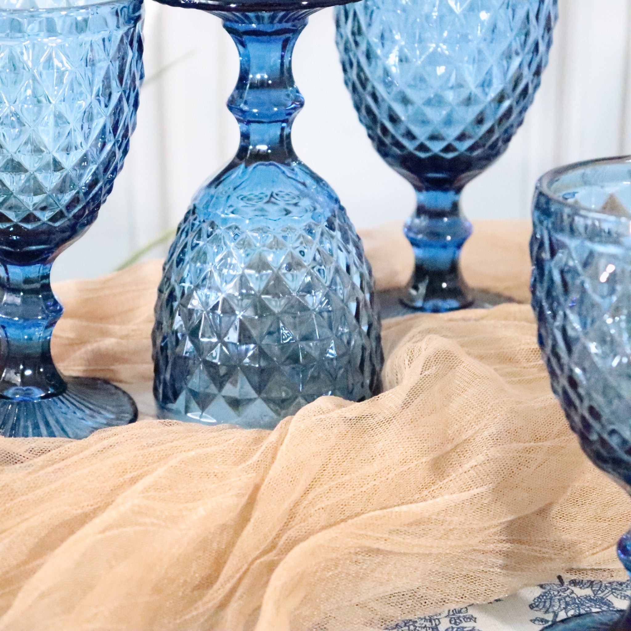Blue textured glass goblets on a beige cloth with a white background