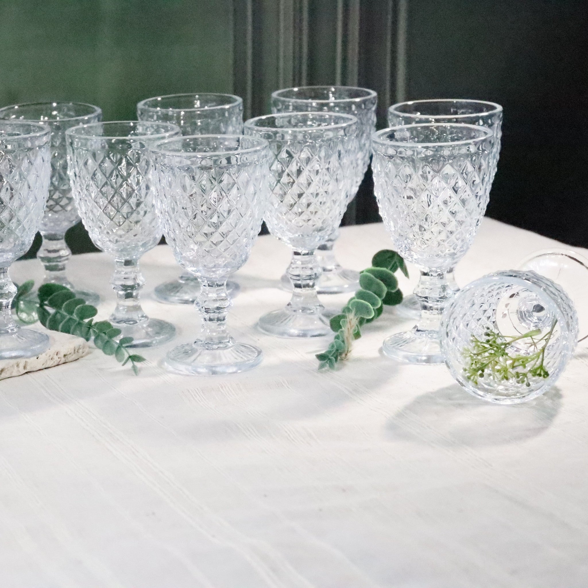 Set of crystal glasses on a white surface with greenery