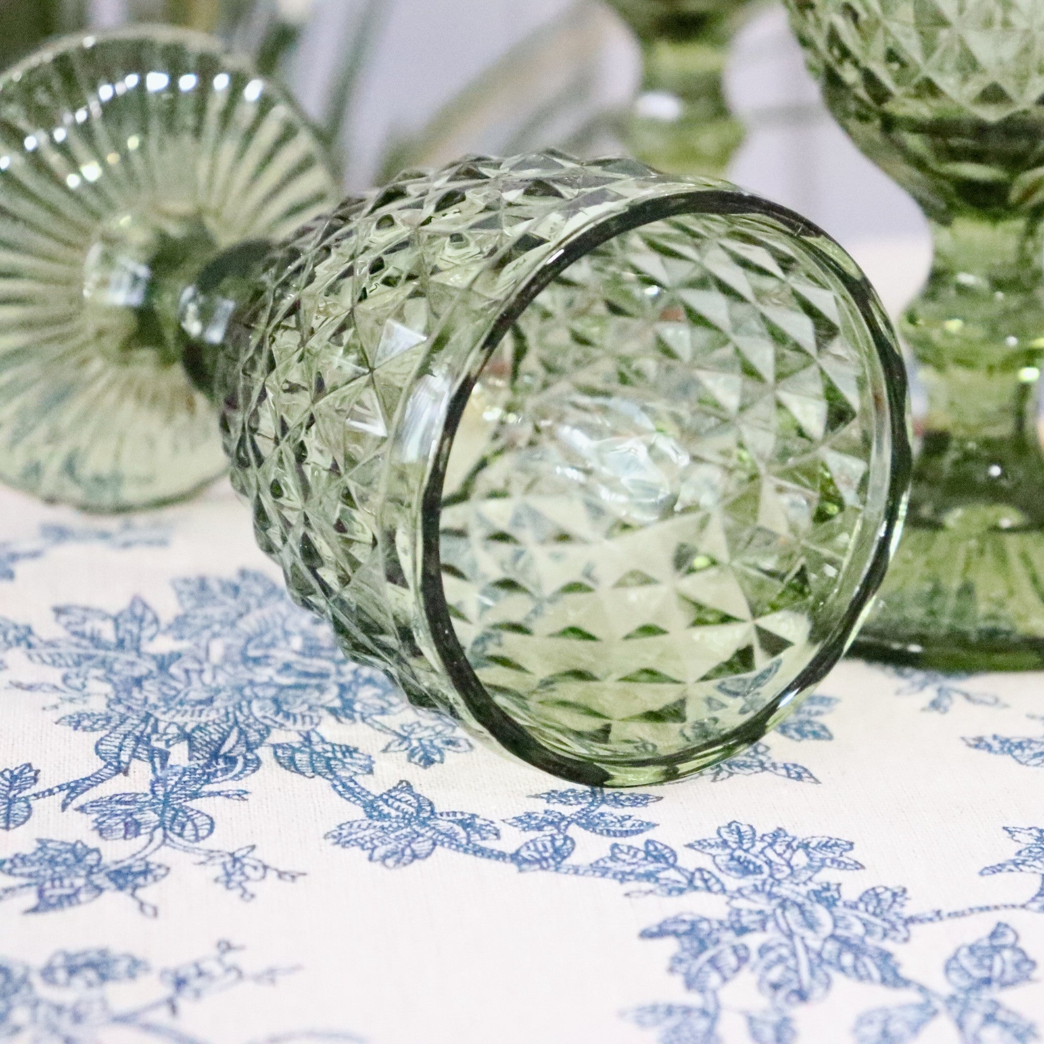 Green glass vase with intricate patterns on a floral tablecloth