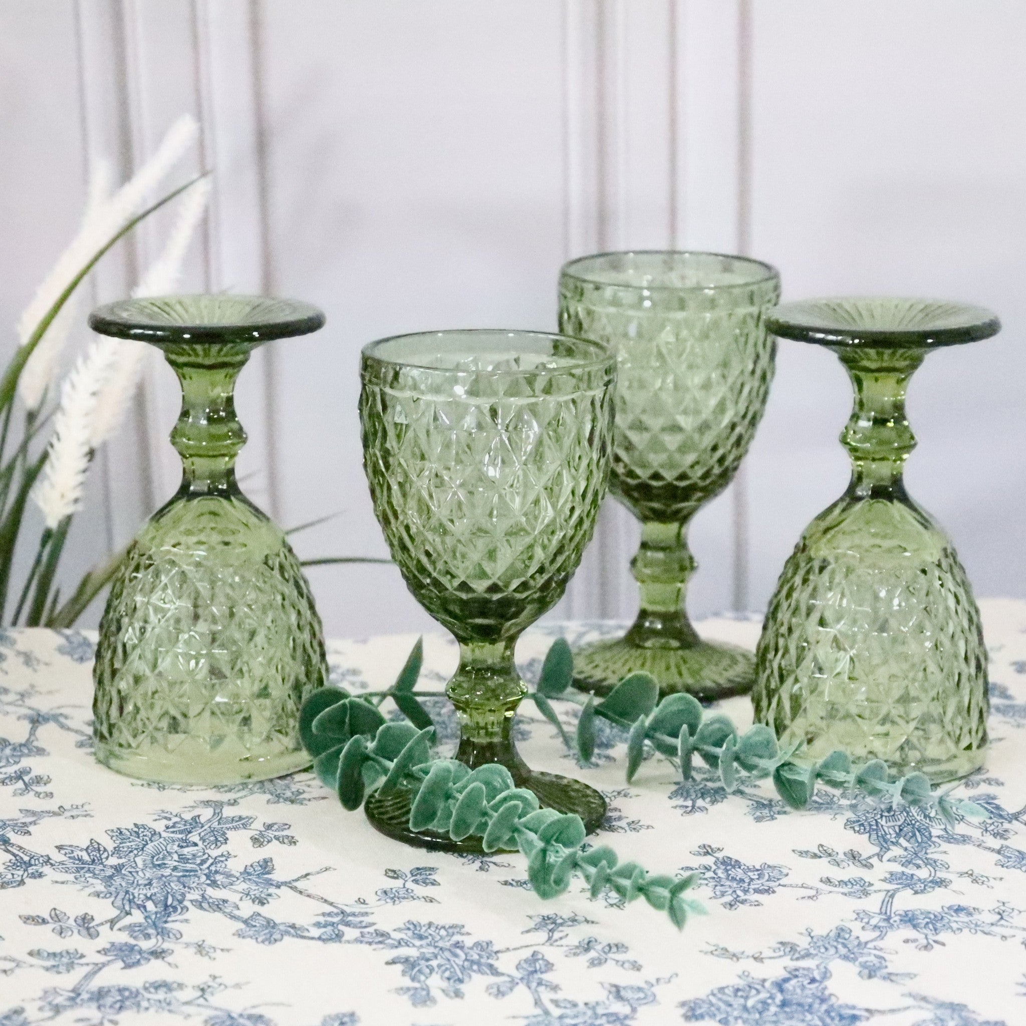 Set of green textured glass goblets on a floral tablecloth with white flowers.