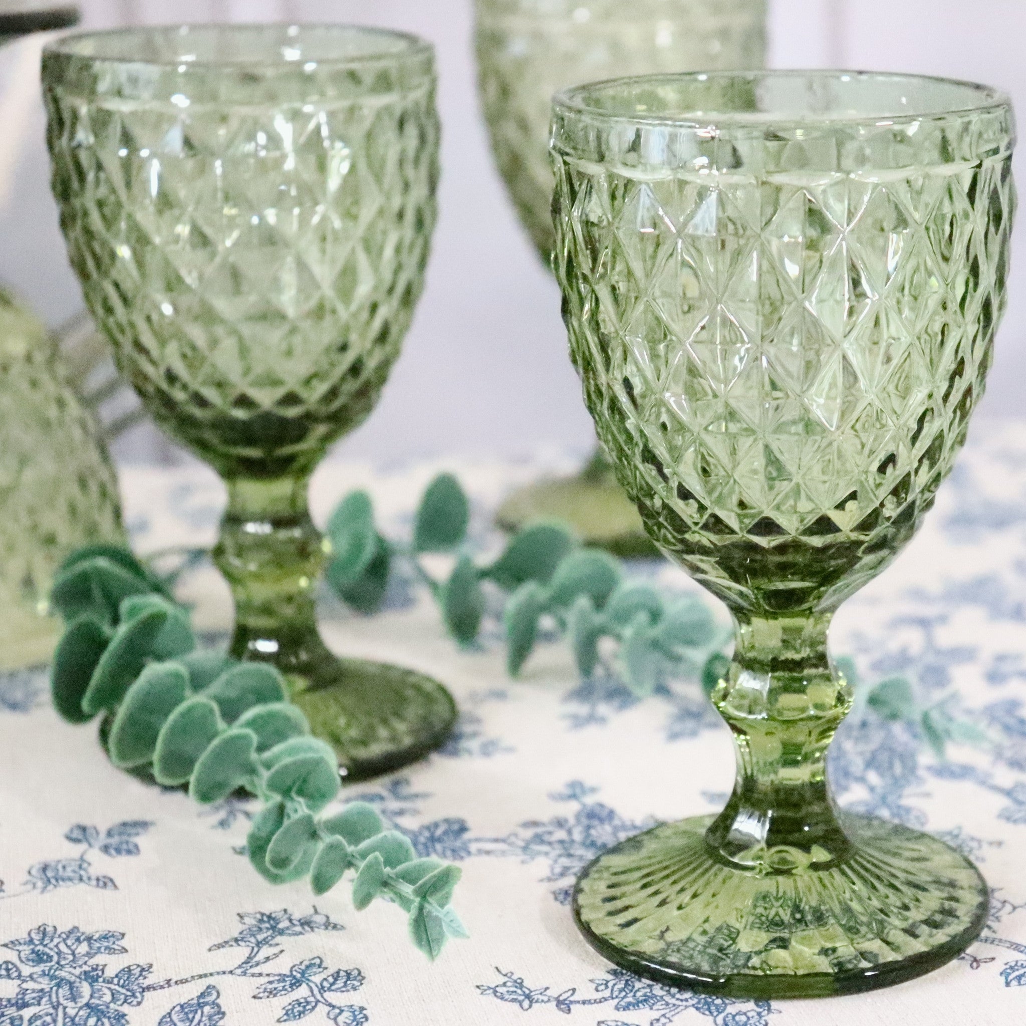 Green glass goblets with textured design on a patterned tablecloth
