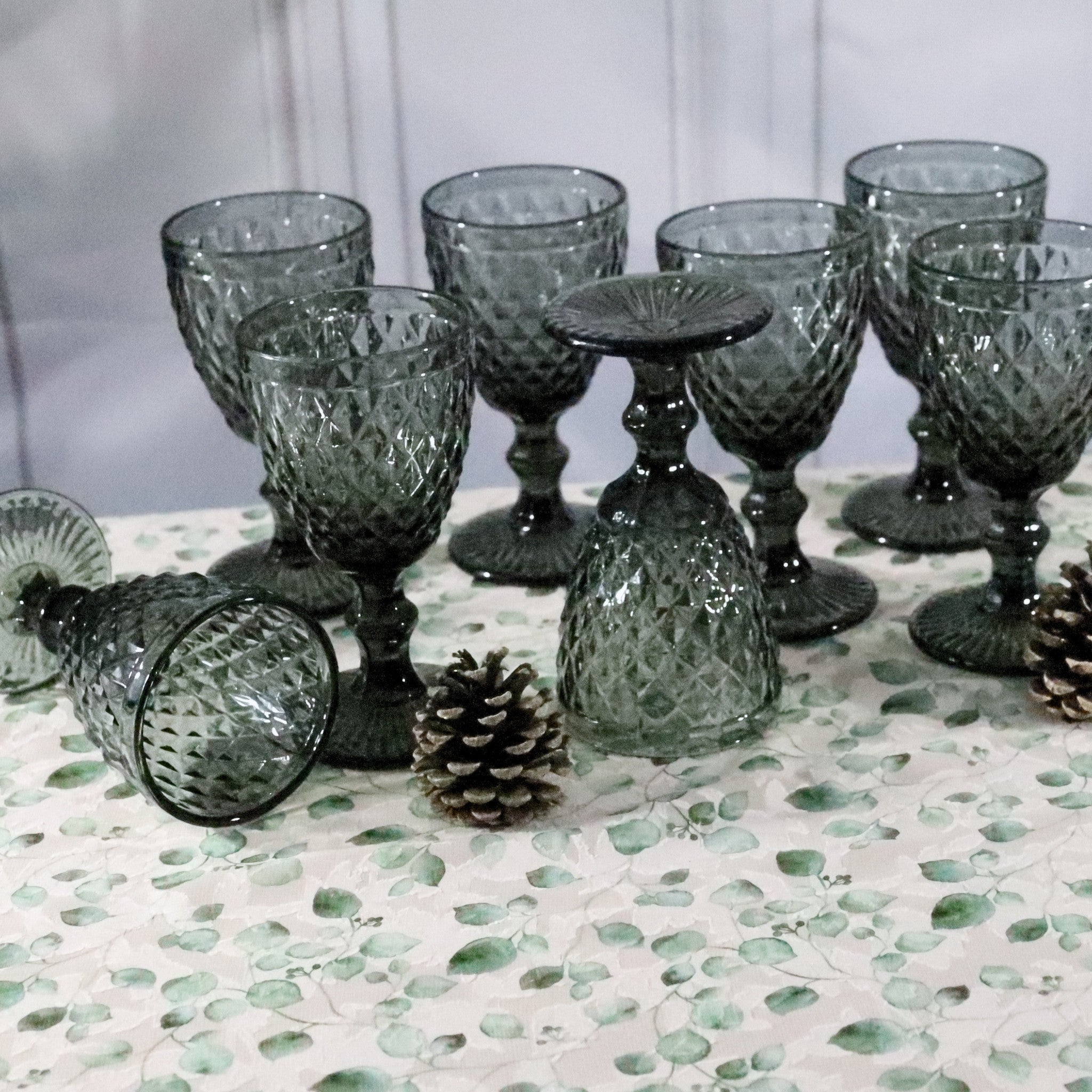 Set of textured glass goblets on a decorative surface with pinecones.