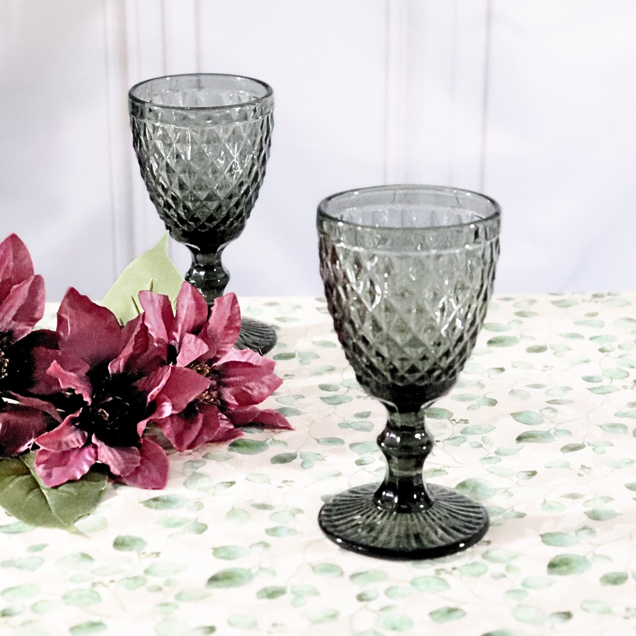 Two textured glass goblets on a patterned tablecloth with pink flowers.