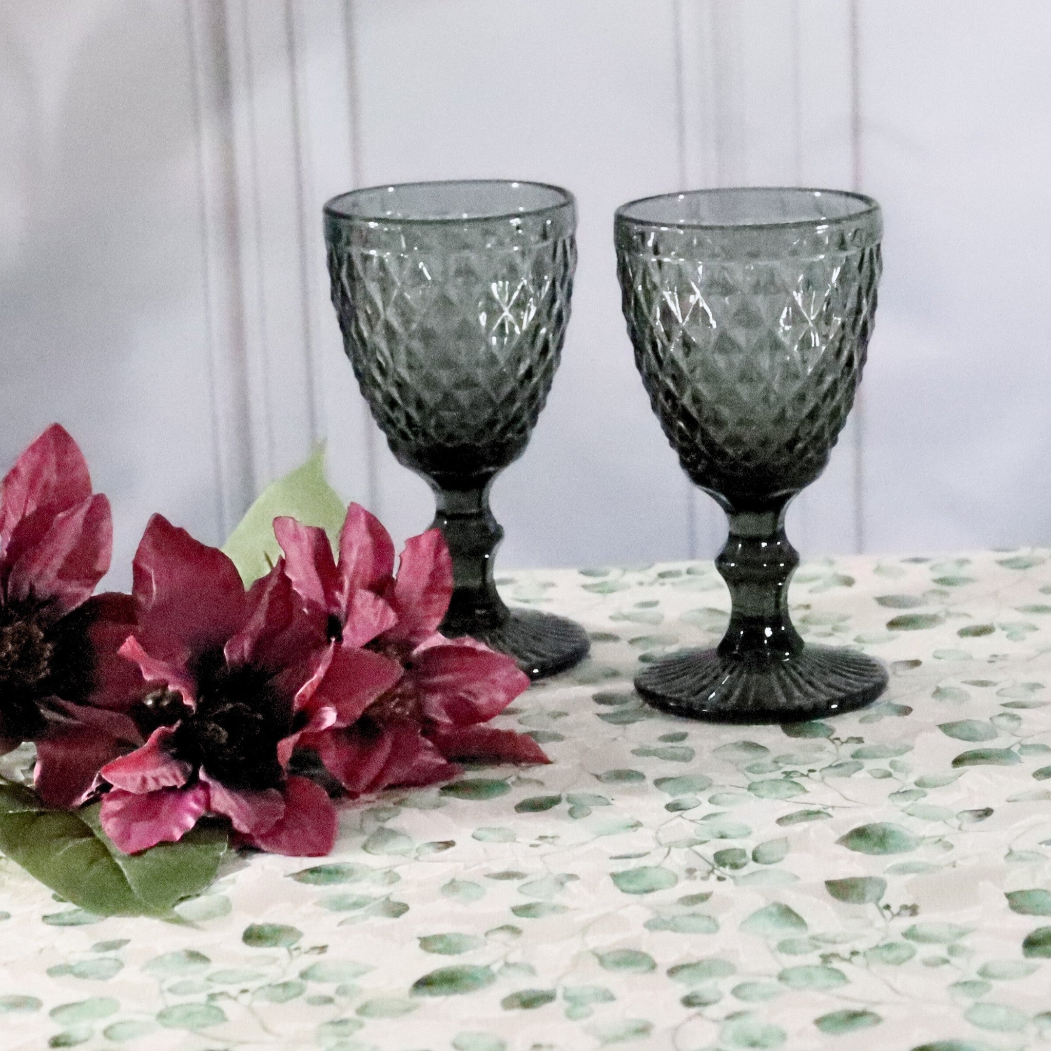 Two gray textured glass goblets on a patterned tablecloth with pink flowers.
