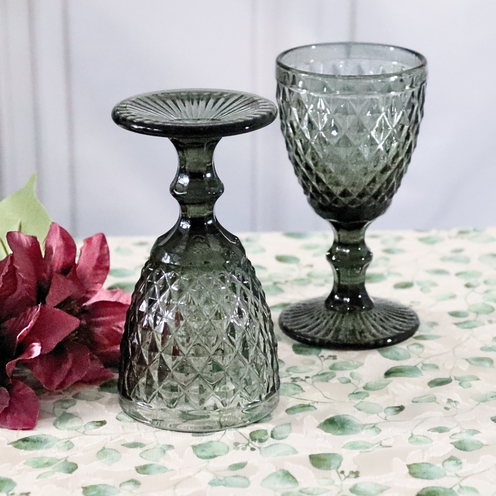 Two grey glass goblets on a patterned surface with pink flowers.