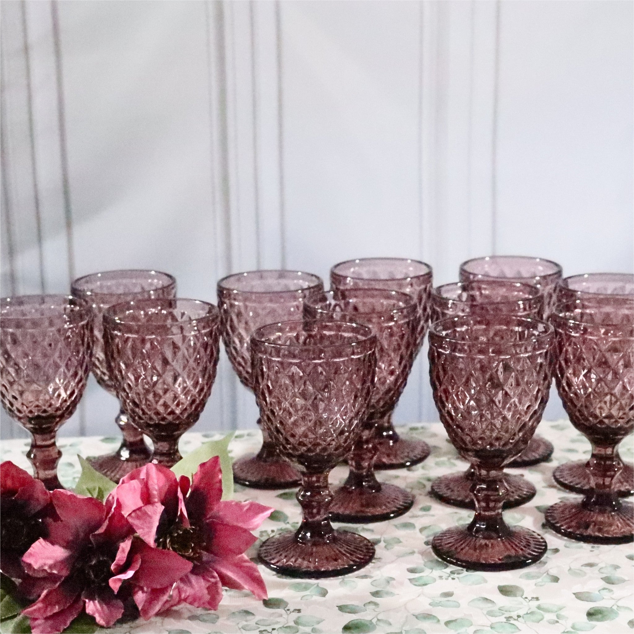Set of purple glass goblets on a table with flowers