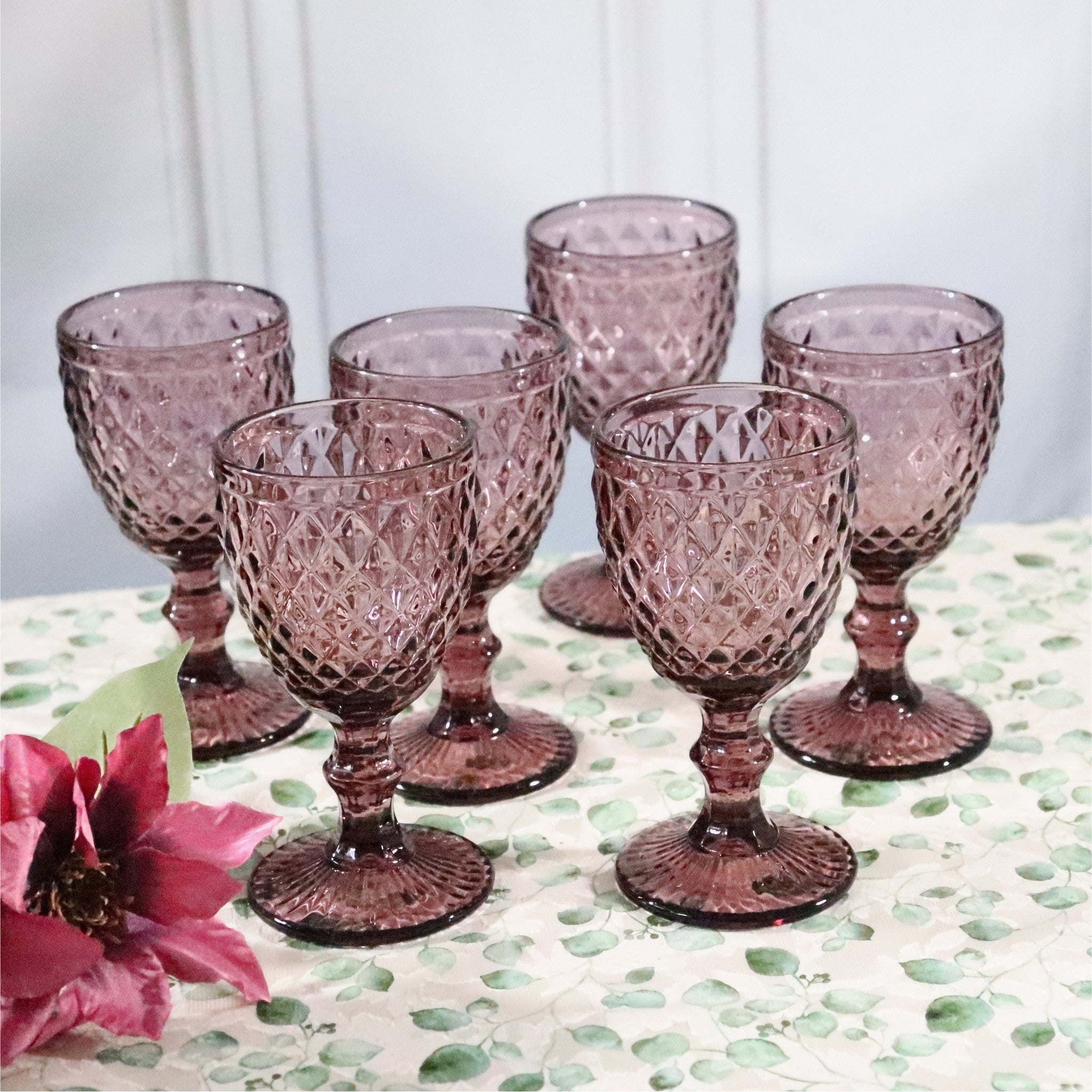 Set of six purple glass goblets on a patterned surface with flowers.