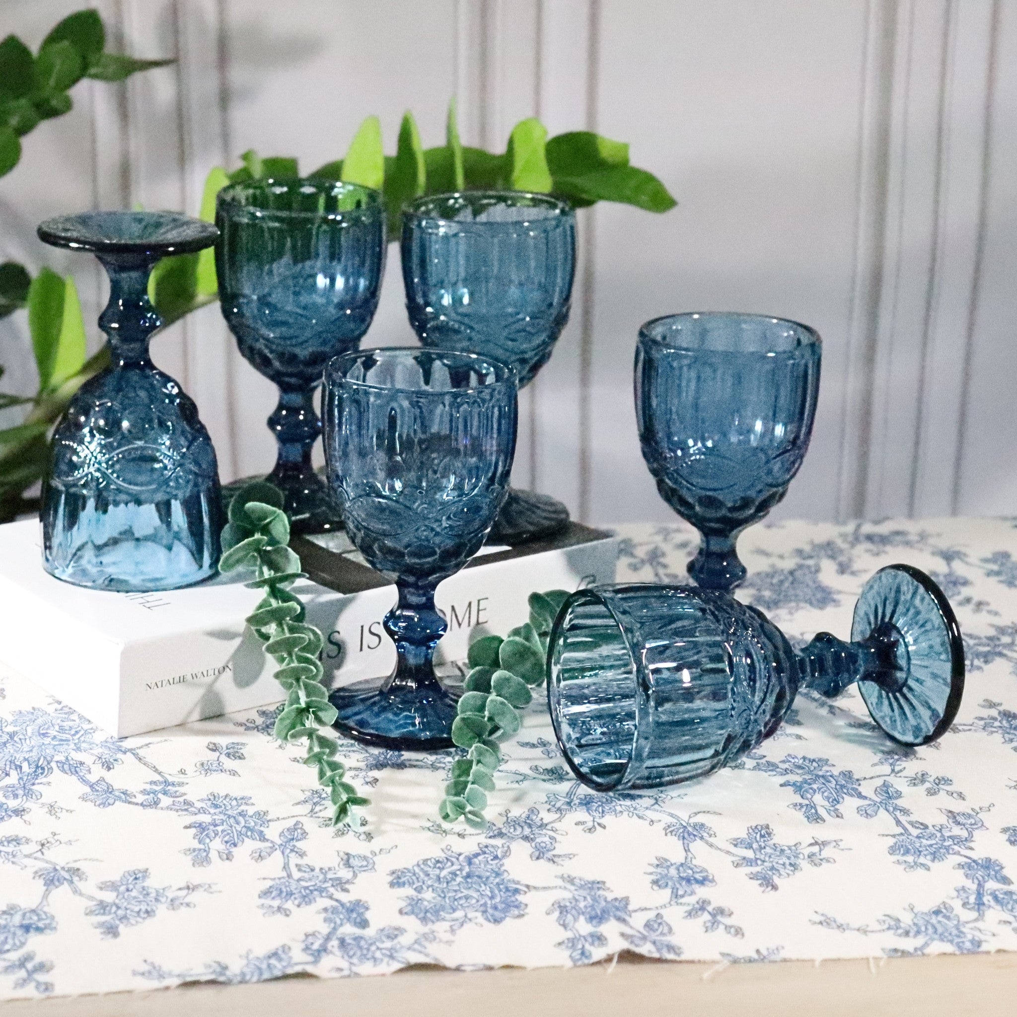 Set of blue glass goblets on a floral tablecloth with greenery in the background