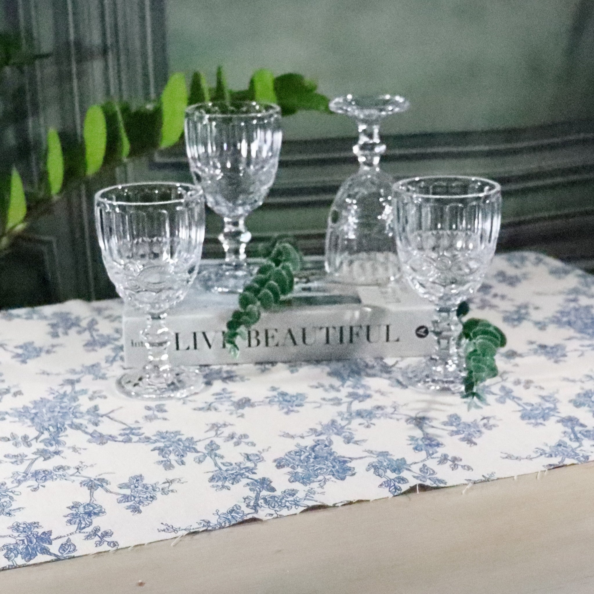 Clear glassware on a floral tablecloth with a book titled 'Live Beautiful'.