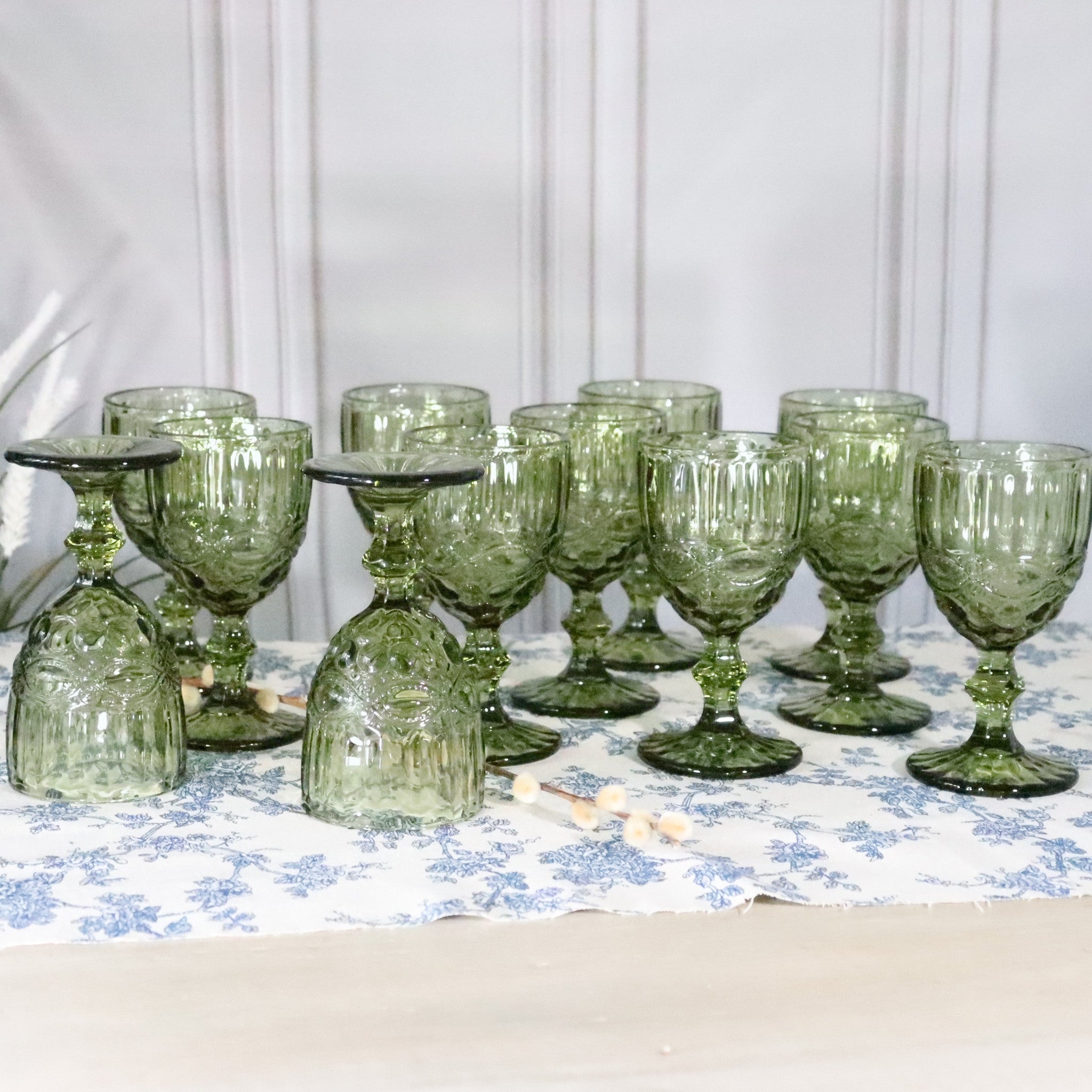 Set of green glass goblets on a floral tablecloth with a white background