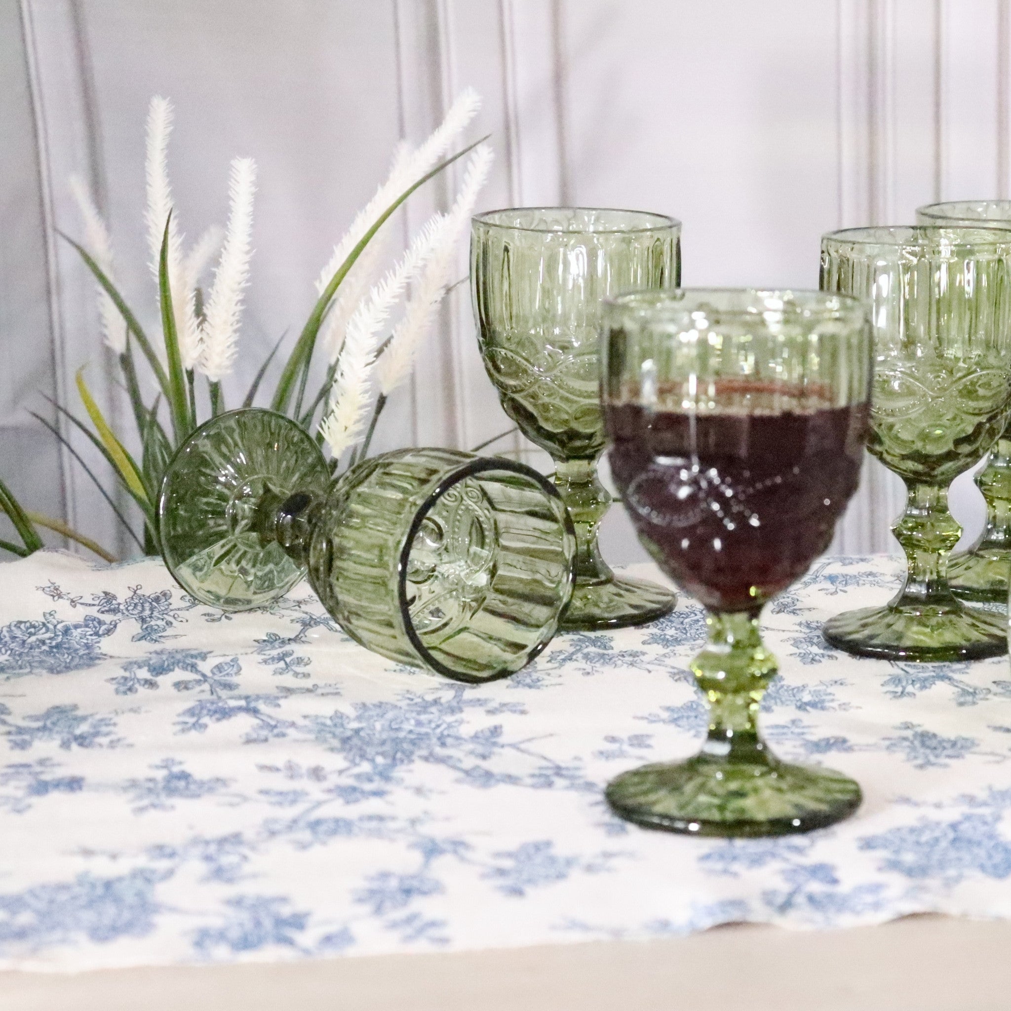 Green glass goblets on a floral tablecloth with a white background