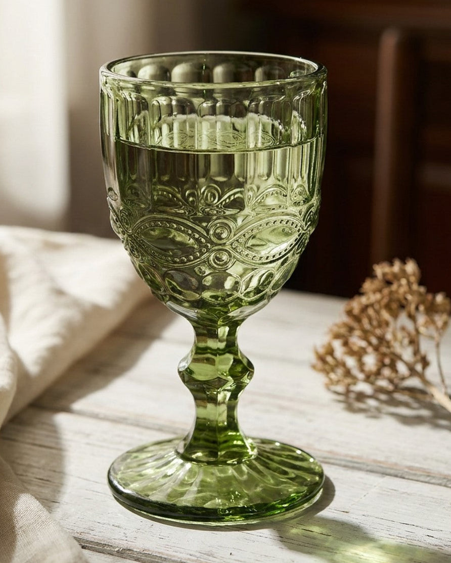 Two green glass goblets on a floral tablecloth with a white background