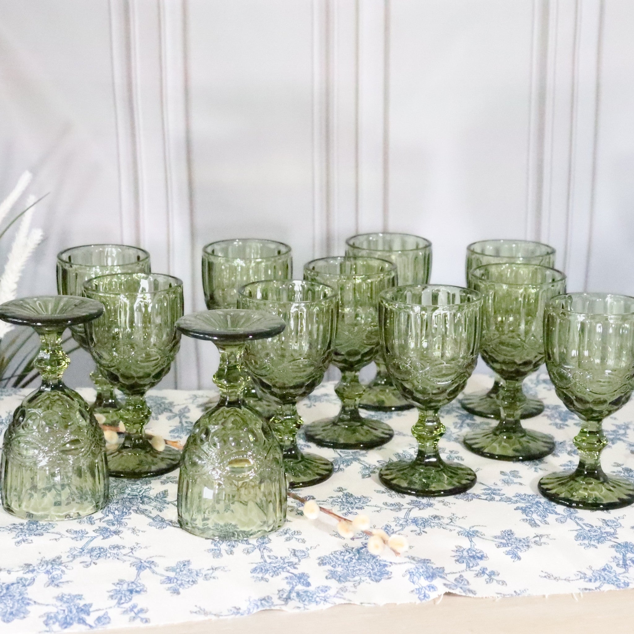 Set of green glass goblets on a floral tablecloth with a white background