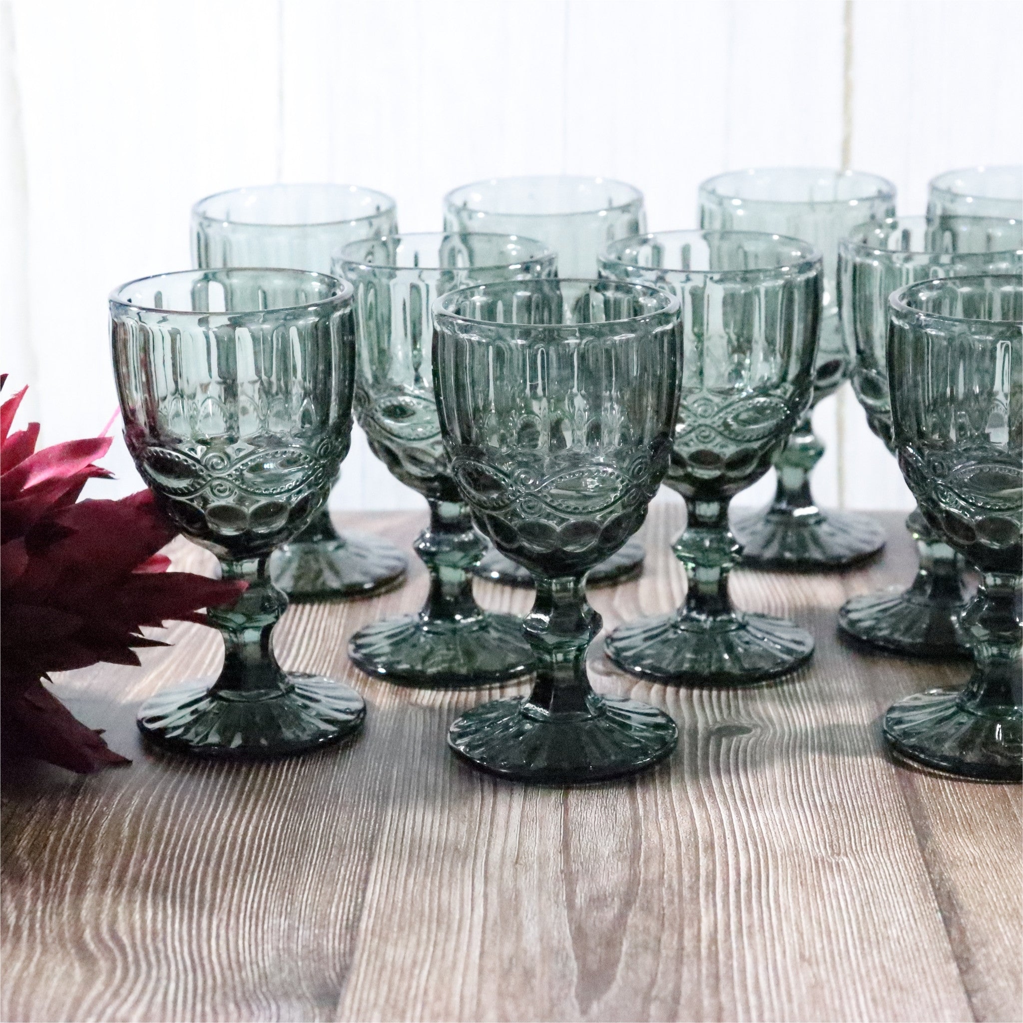 Set of grey glass goblets on a wooden table with a pink flower.