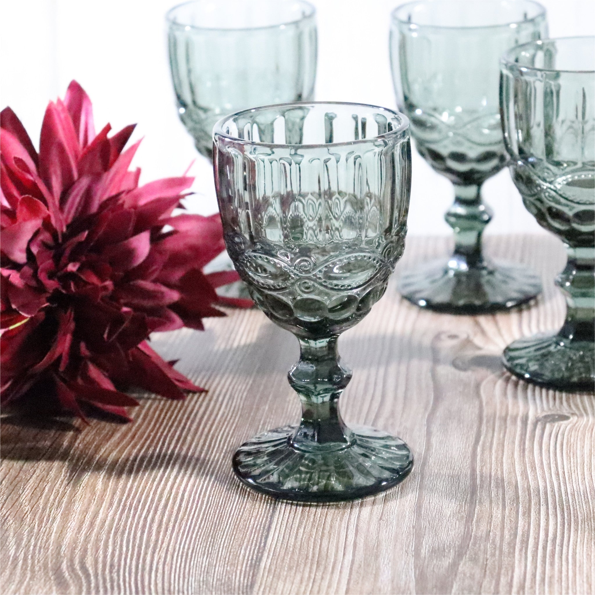 Decorative glass goblets on a wooden surface with a pink flower.