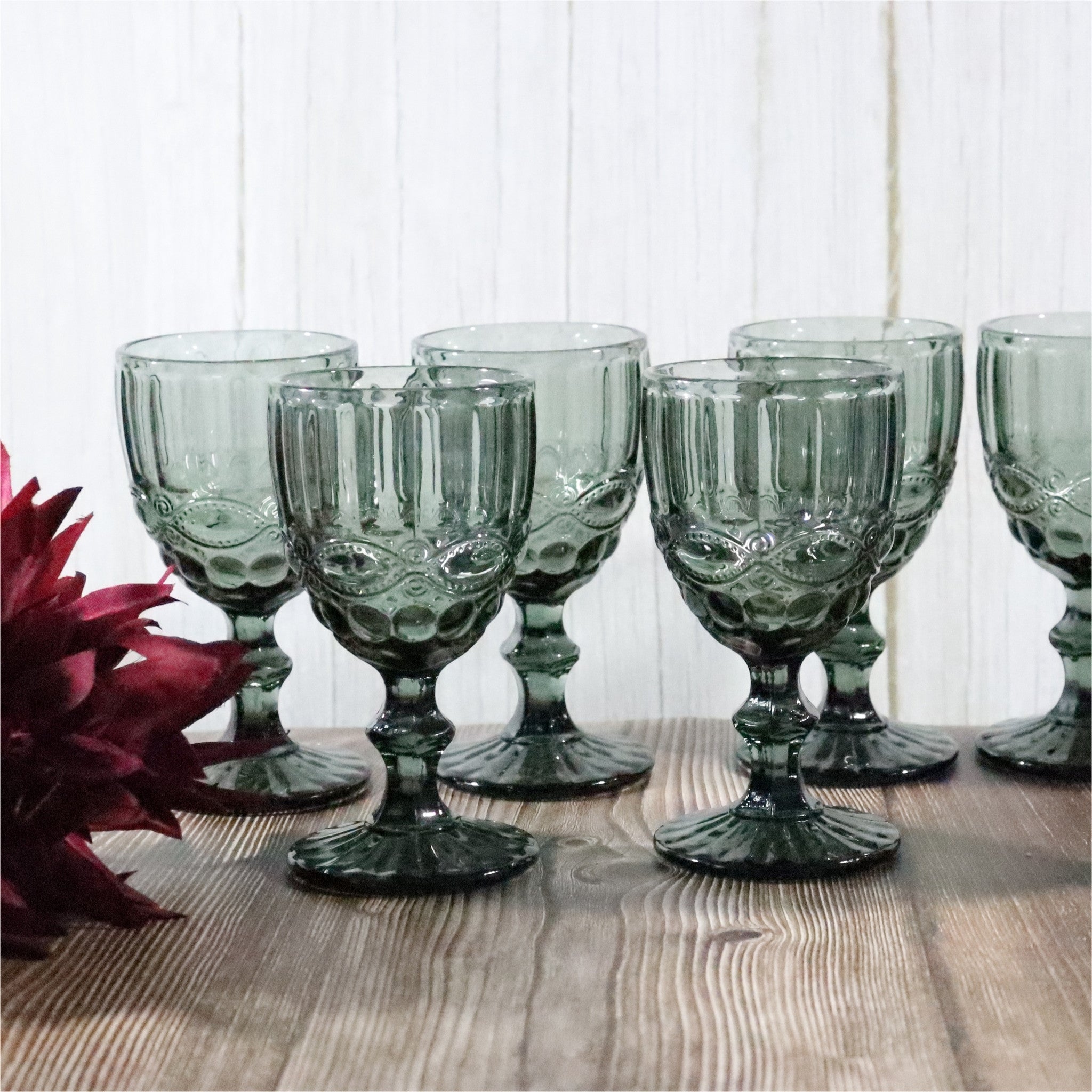 Set of grey glass goblets on a wooden surface with a white paneled background