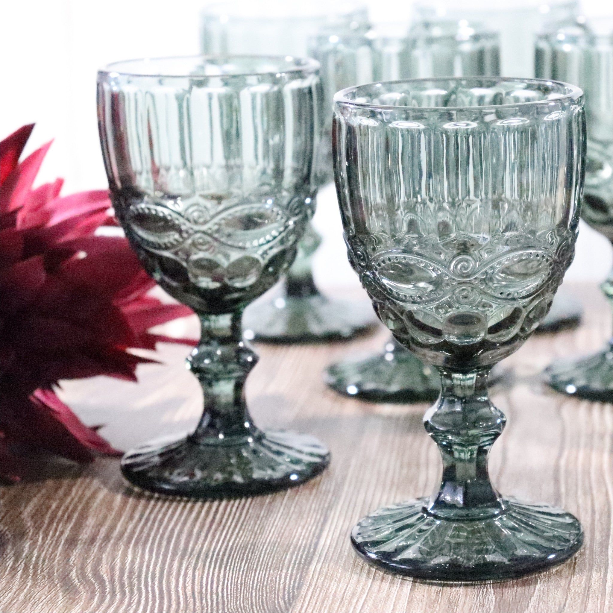 Decorative glass goblets on a wooden surface with flowers in the background
