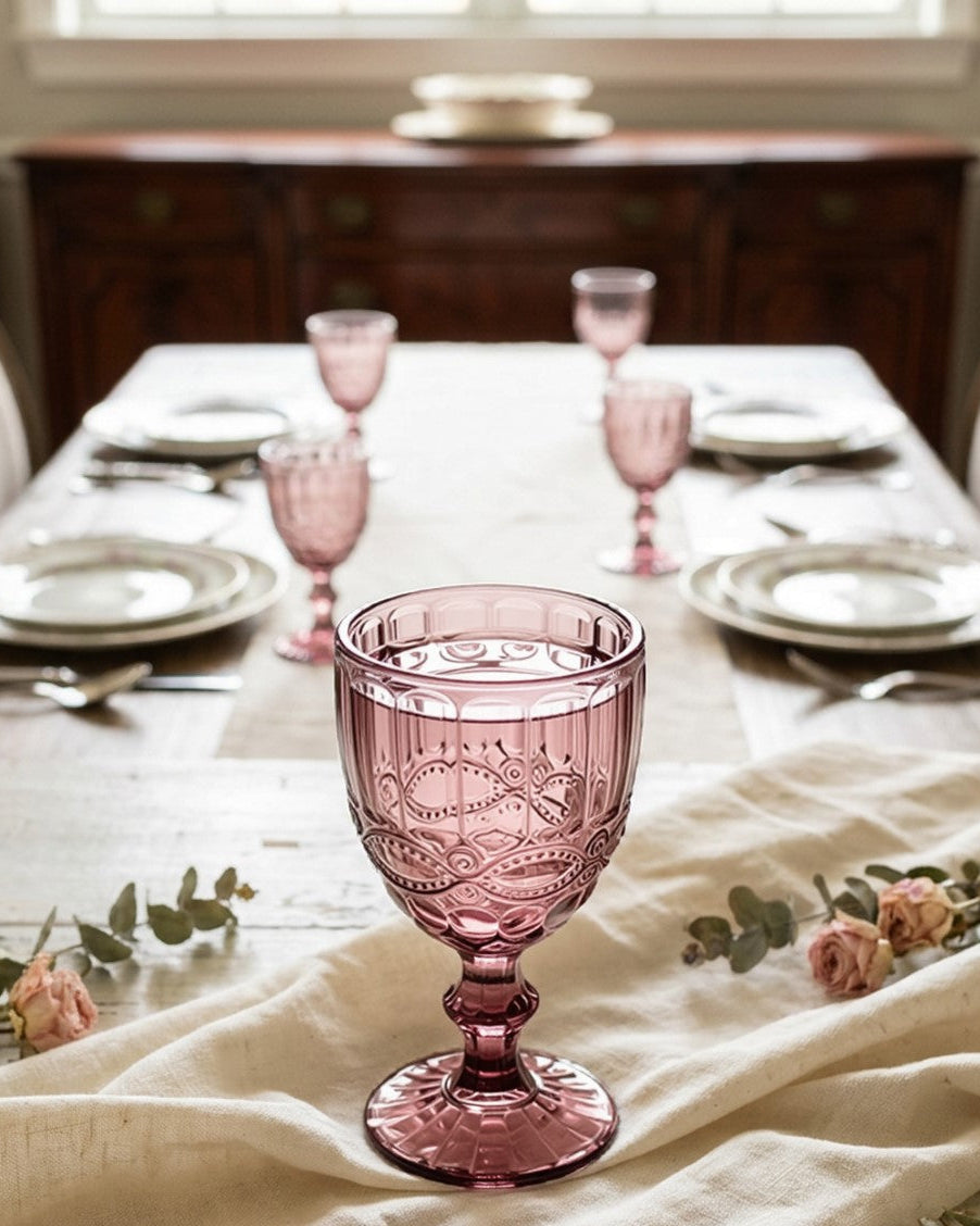 Three pink glass goblets with decorative patterns on a light background