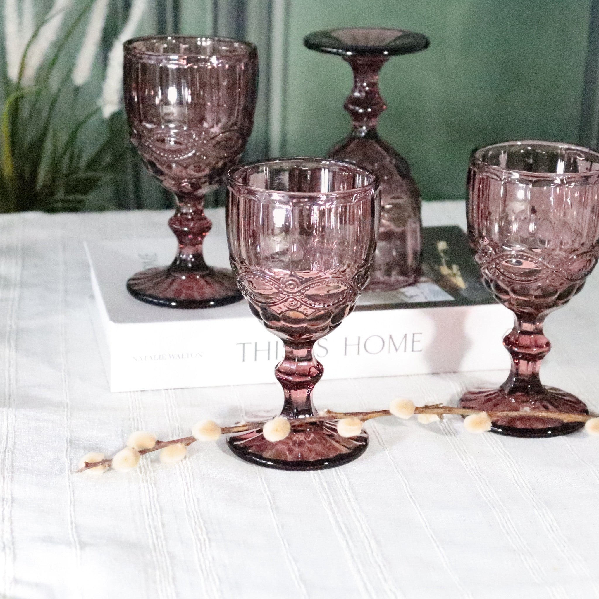 Set of three purple glass goblets on a white surface with a blurred background