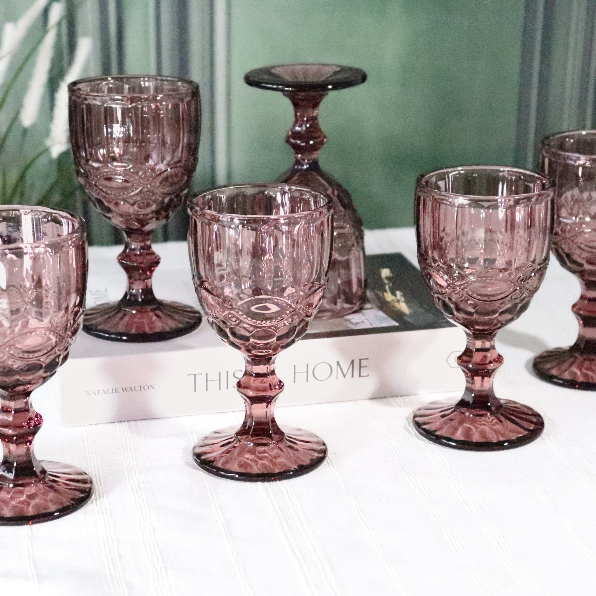 Set of purple glass goblets on a white surface with a blurred green background