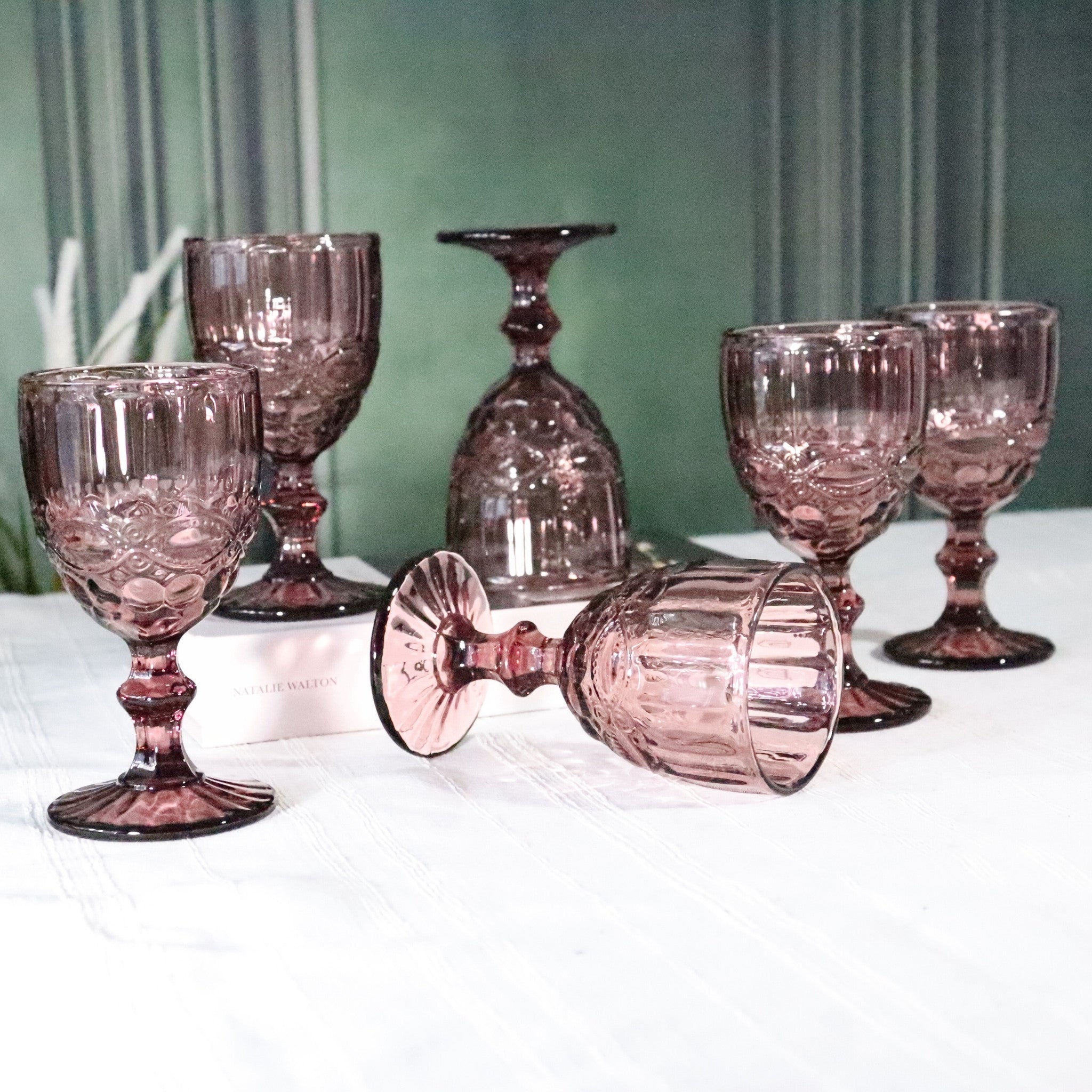Set of purple glass goblets on a white surface with a green curtain background