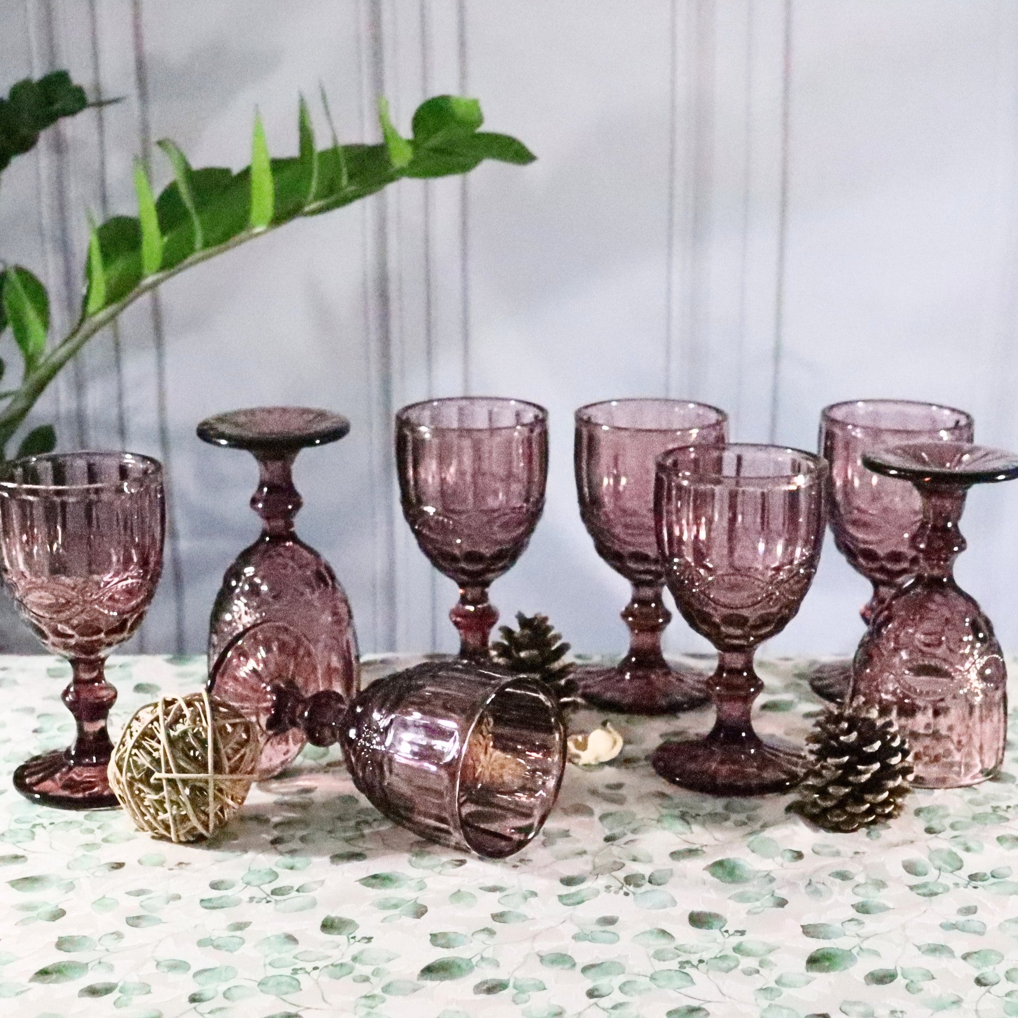Set of pink glass goblets on a decorative table with greenery.