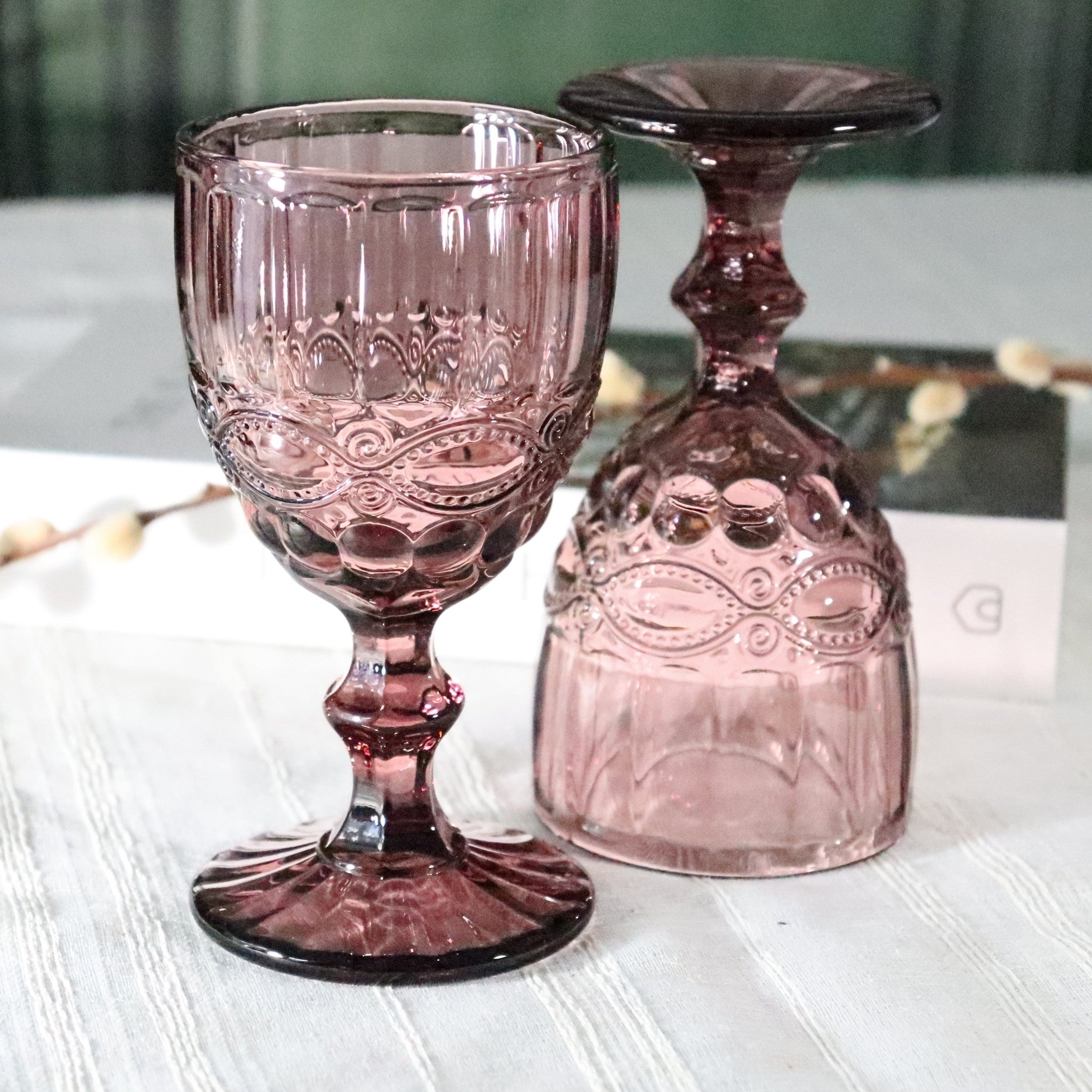 Two purple glass goblets with intricate designs on a white surface.