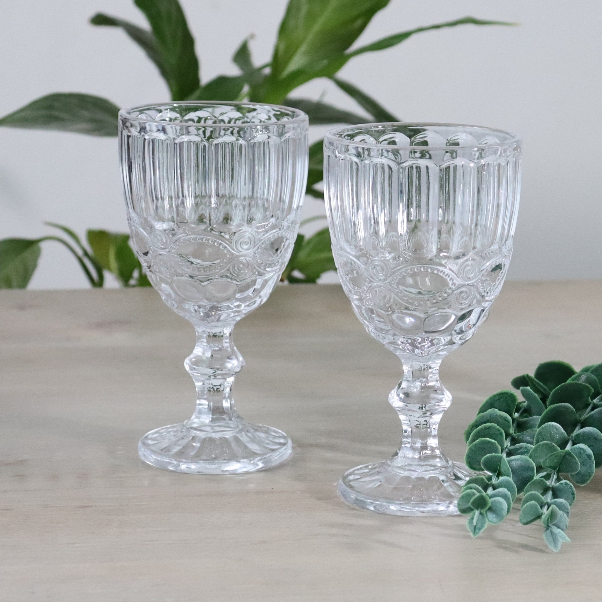 Set of four clear glass goblets on a wooden surface with greenery in the background