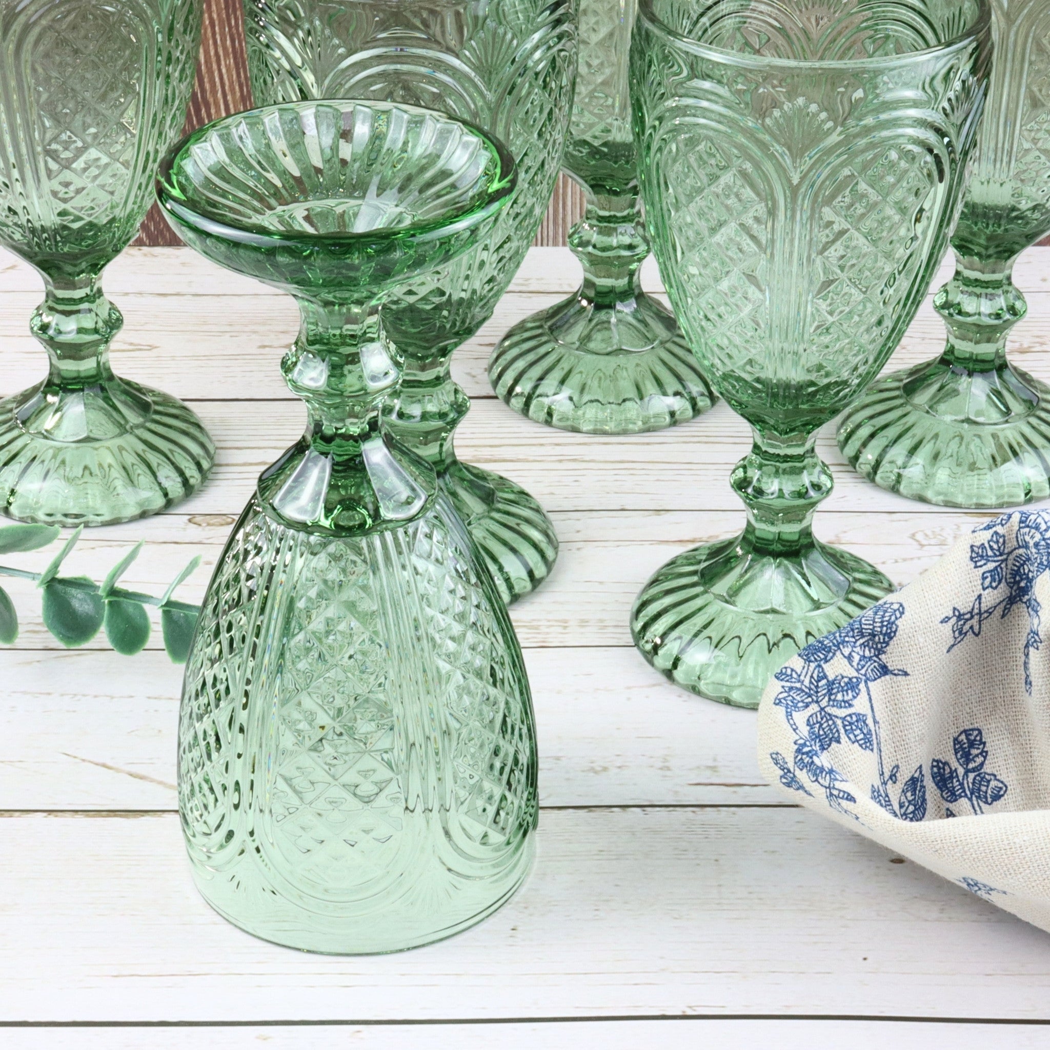 Set of green glass goblets on a white surface with flowers and a decorative box in the background.