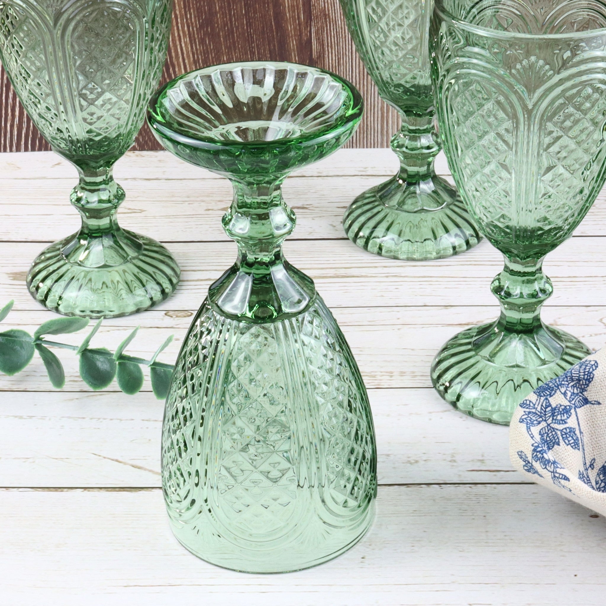 Set of green glass goblets on a white surface with a red flower.