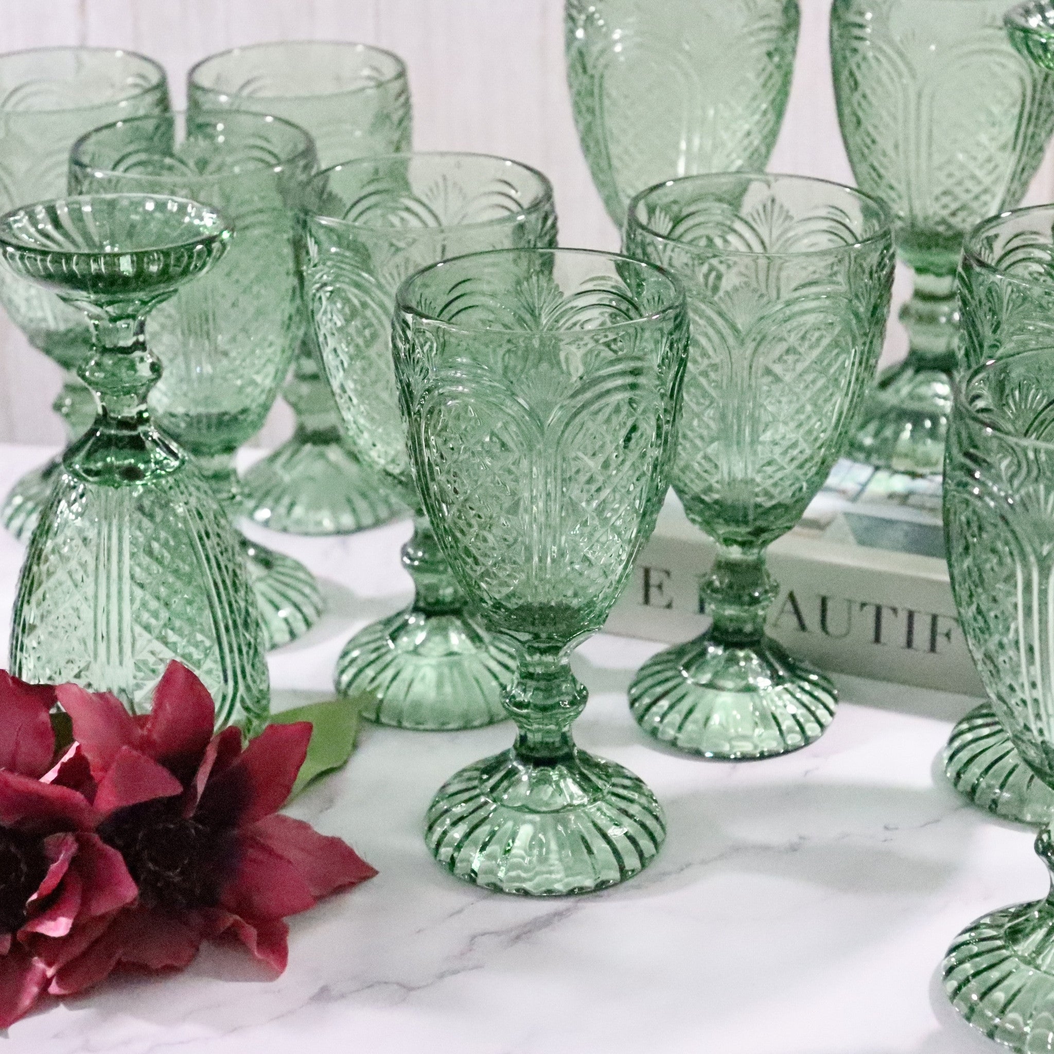 Set of green glass goblets with floral design on a marble surface.