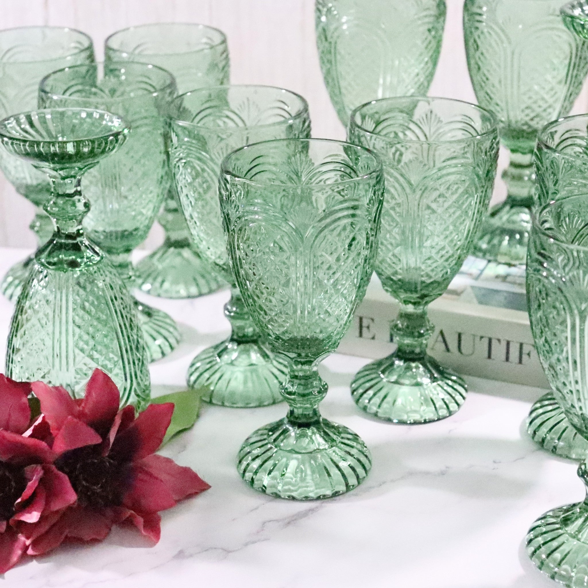 Set of green patterned glass goblets on a white surface with a blurred book in the background.