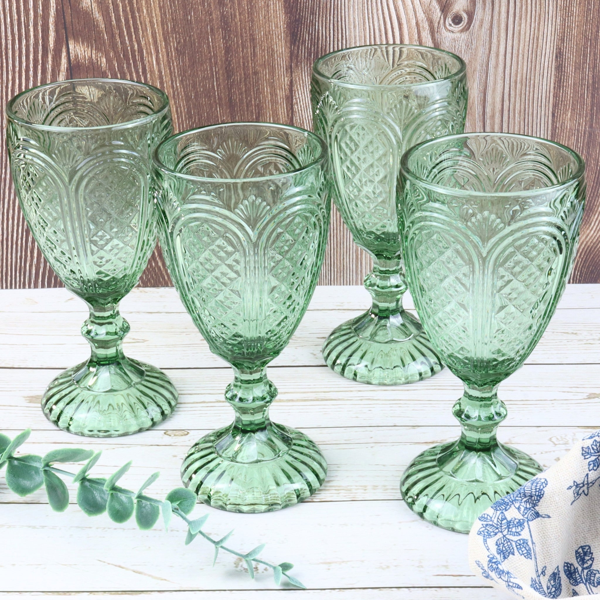Set of green glass goblets on a white surface with red flowers and a book in the background.