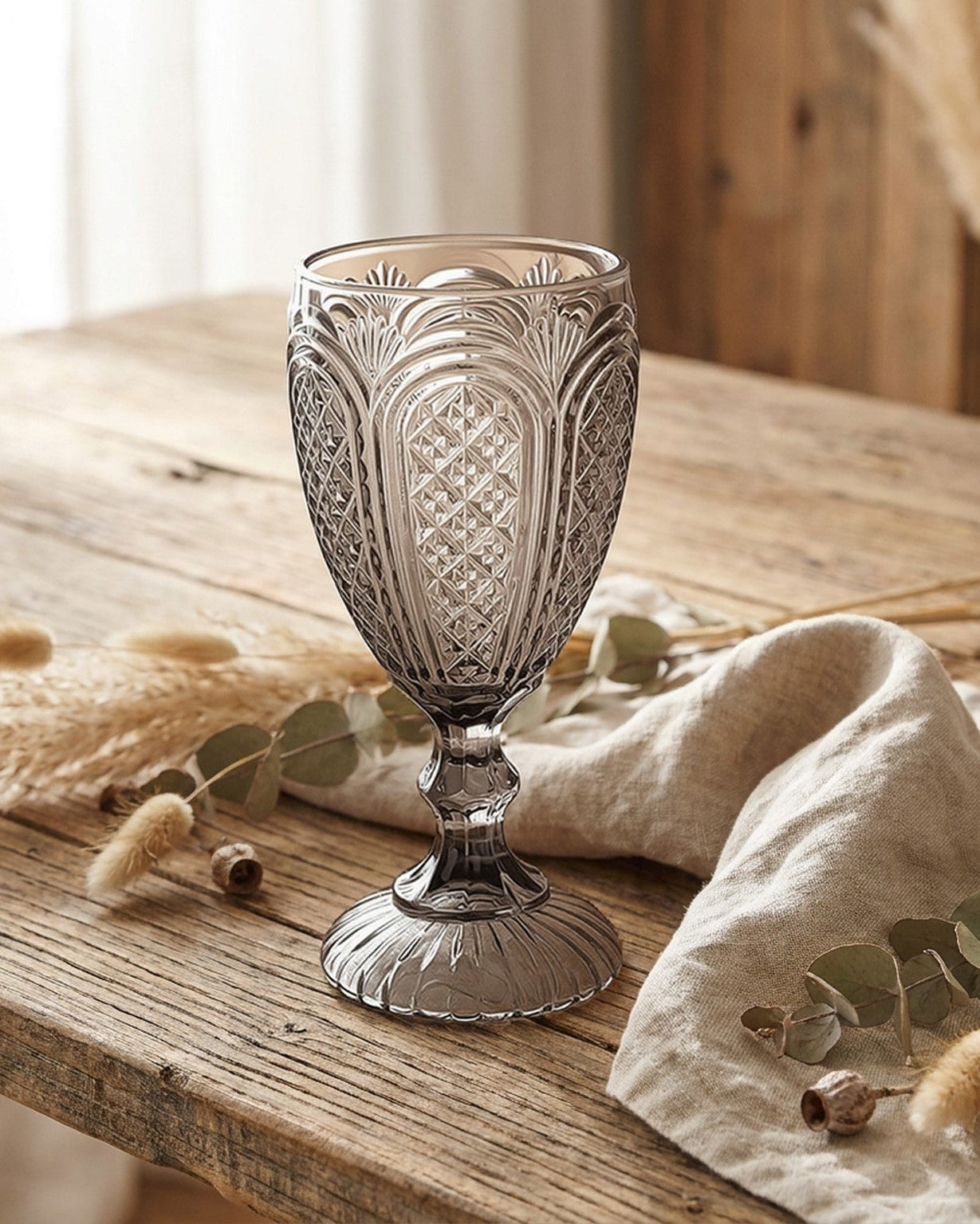 Set of grey glass goblets on a marble surface with a decorative book and flowers in the background.