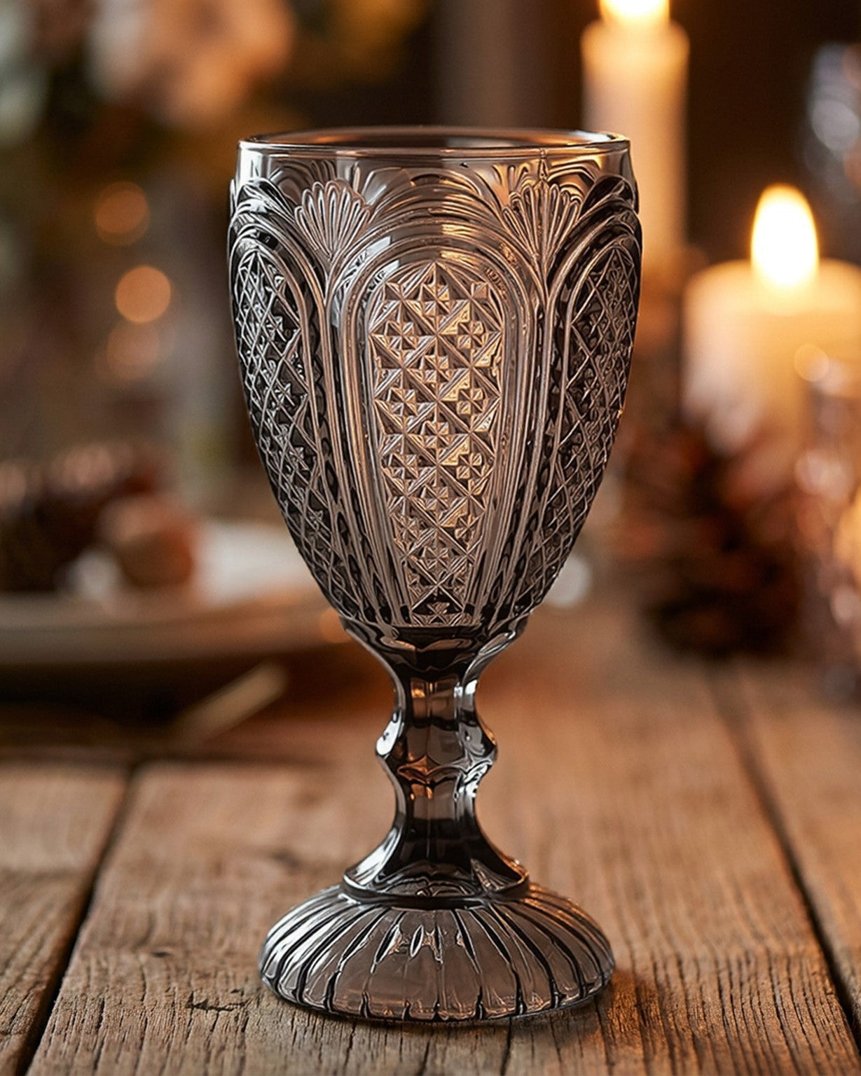 Two patterned glass goblets on a wooden surface with greenery in the background