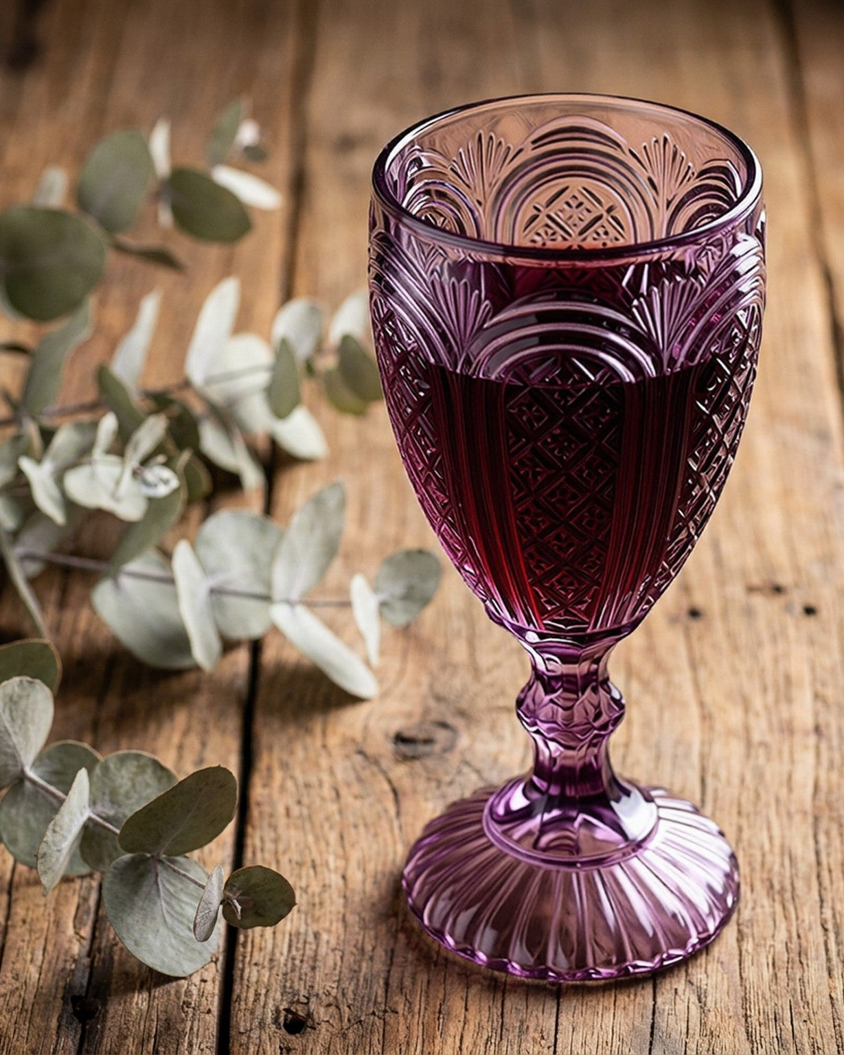 Set of five purple glass goblets on a white surface with a floral arrangement.