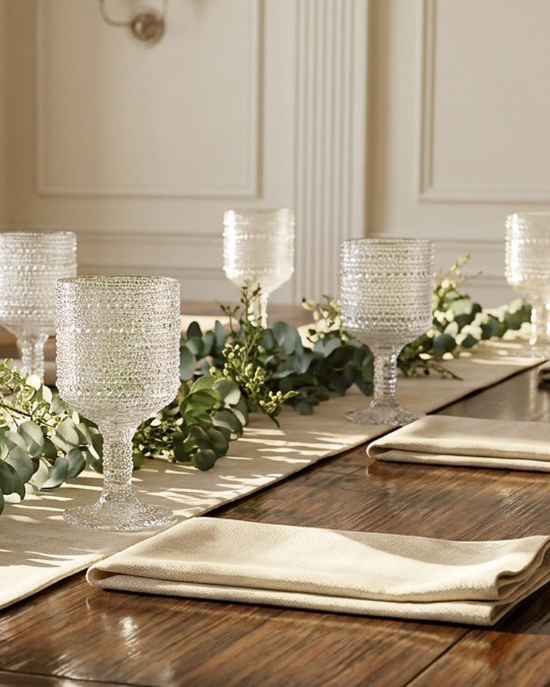 Elegant dining table setting with glasses, napkins, and greenery in a well-lit room.