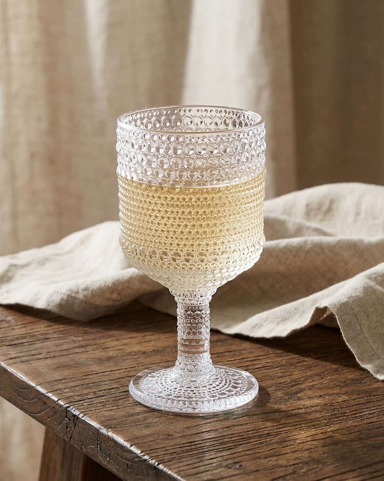 Two textured glass goblets on a wooden surface with a beige cloth.